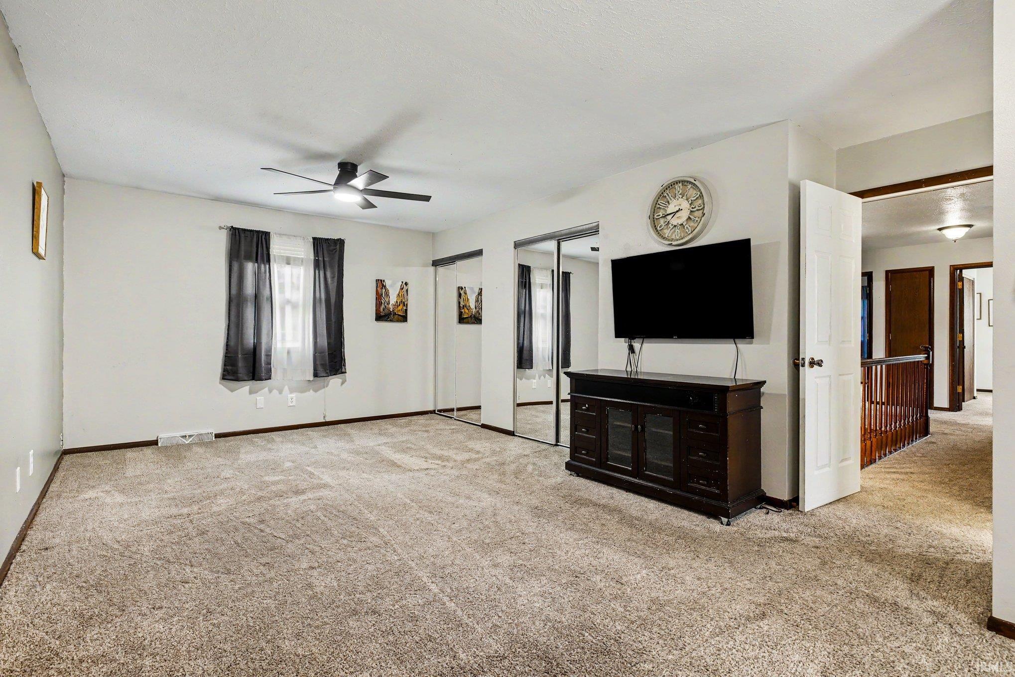 Spacious room featuring neutral carpeting, a ceiling fan, and sliding mirrored closet doors