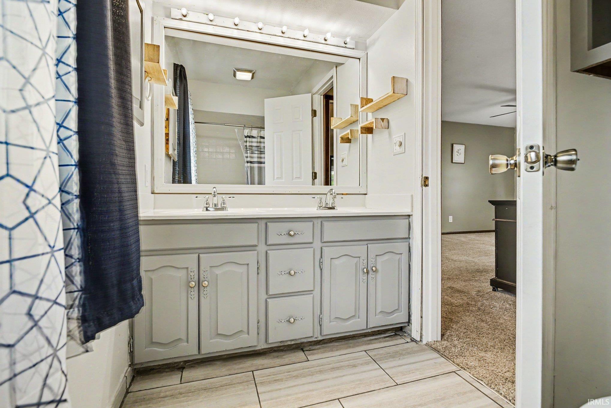 Bathroom vanity featuring dual sinks with individual faucets, ample storage cabinetry, and an expansive mirror with overhead lighting