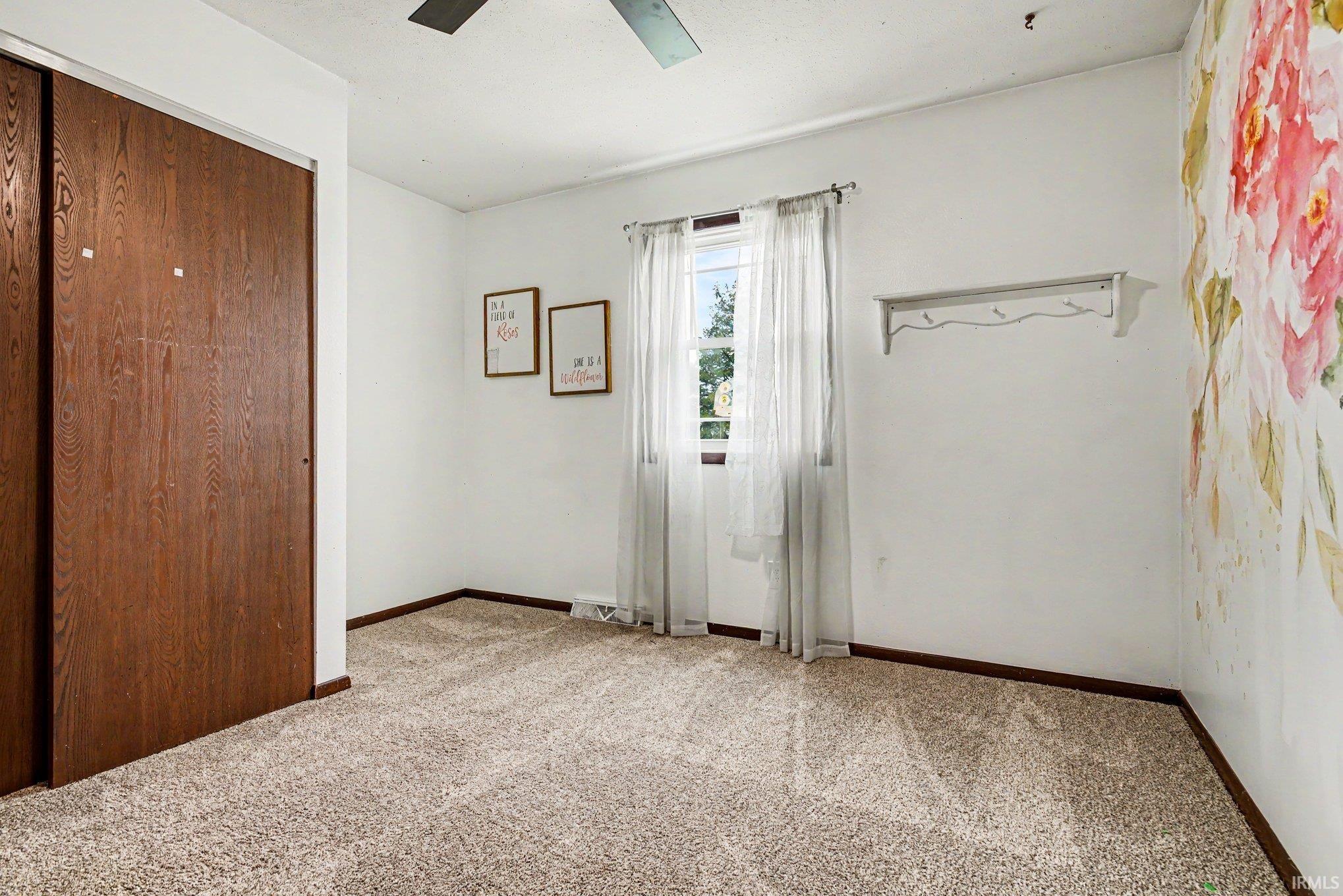 Carpeted room featuring a window with sheer curtains, a ceiling fan, and a wall-mounted hook rack