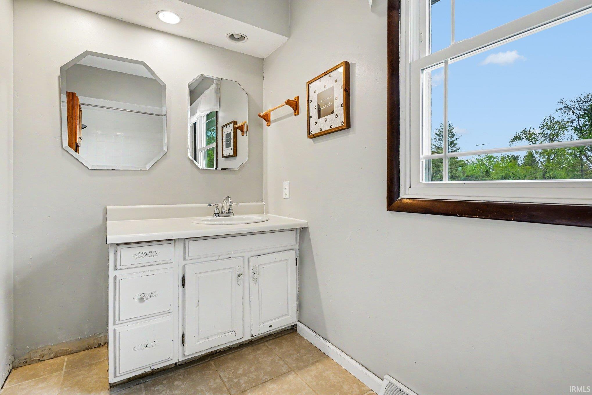 Vanity with integrated sink and chrome faucet, flanked by two octagonal mirrors, set against light gray walls with recessed lighting