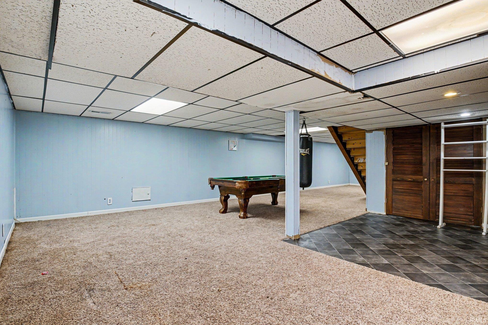 Spacious finished lower level featuring a drop ceiling with recessed lighting, light blue panel walls, and a combination of carpet and dark tile flooring