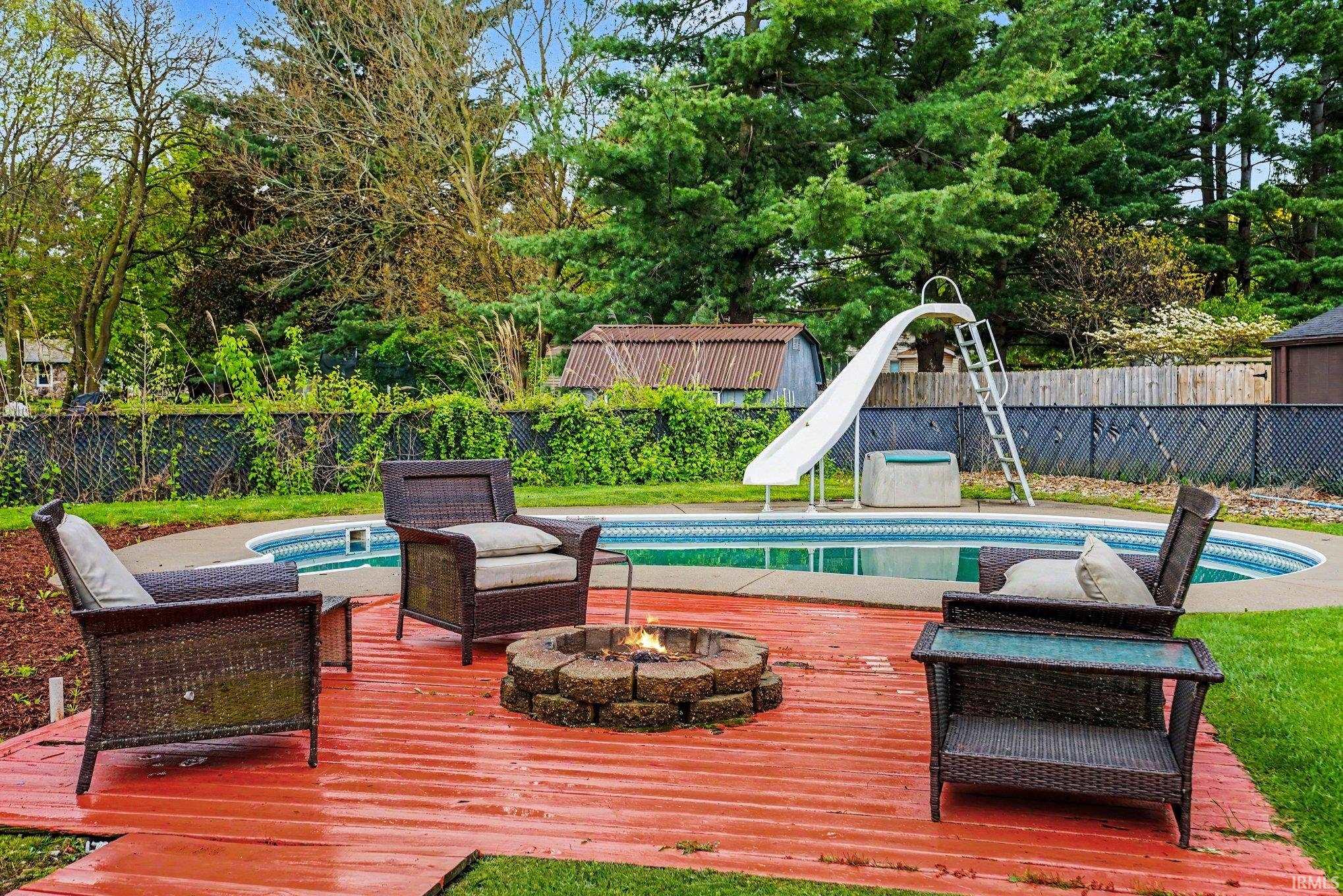 Backyard oasis featuring an oval-shaped pool with a slide, a red-stained wood deck, and a stone-built fire pit