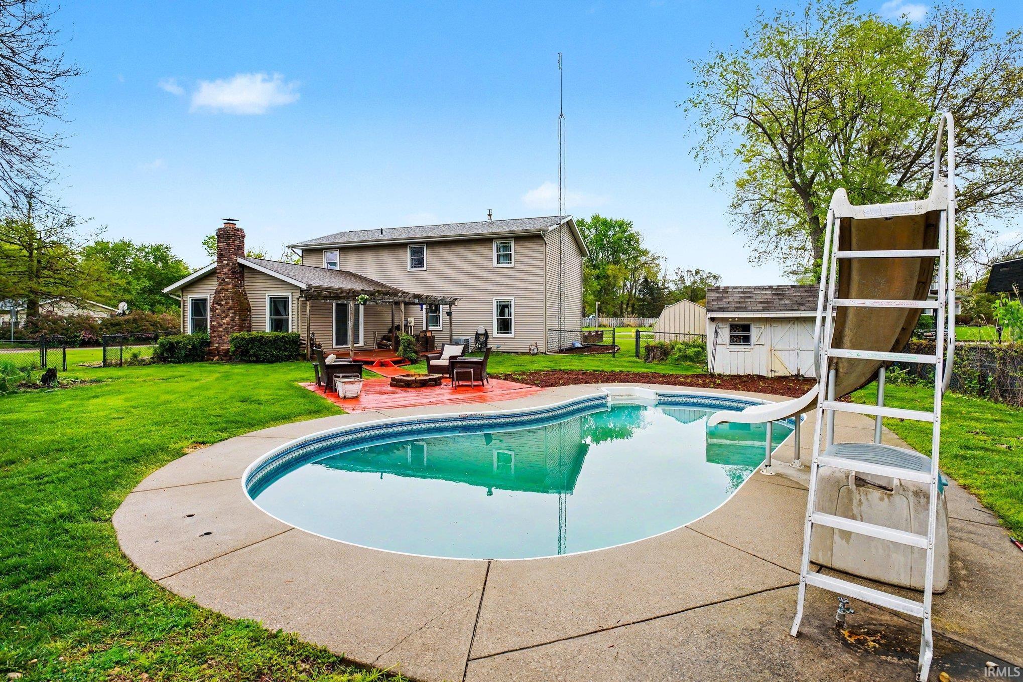 Expansive backyard featuring a freeform swimming pool with a slide, surrounded by a concrete patio