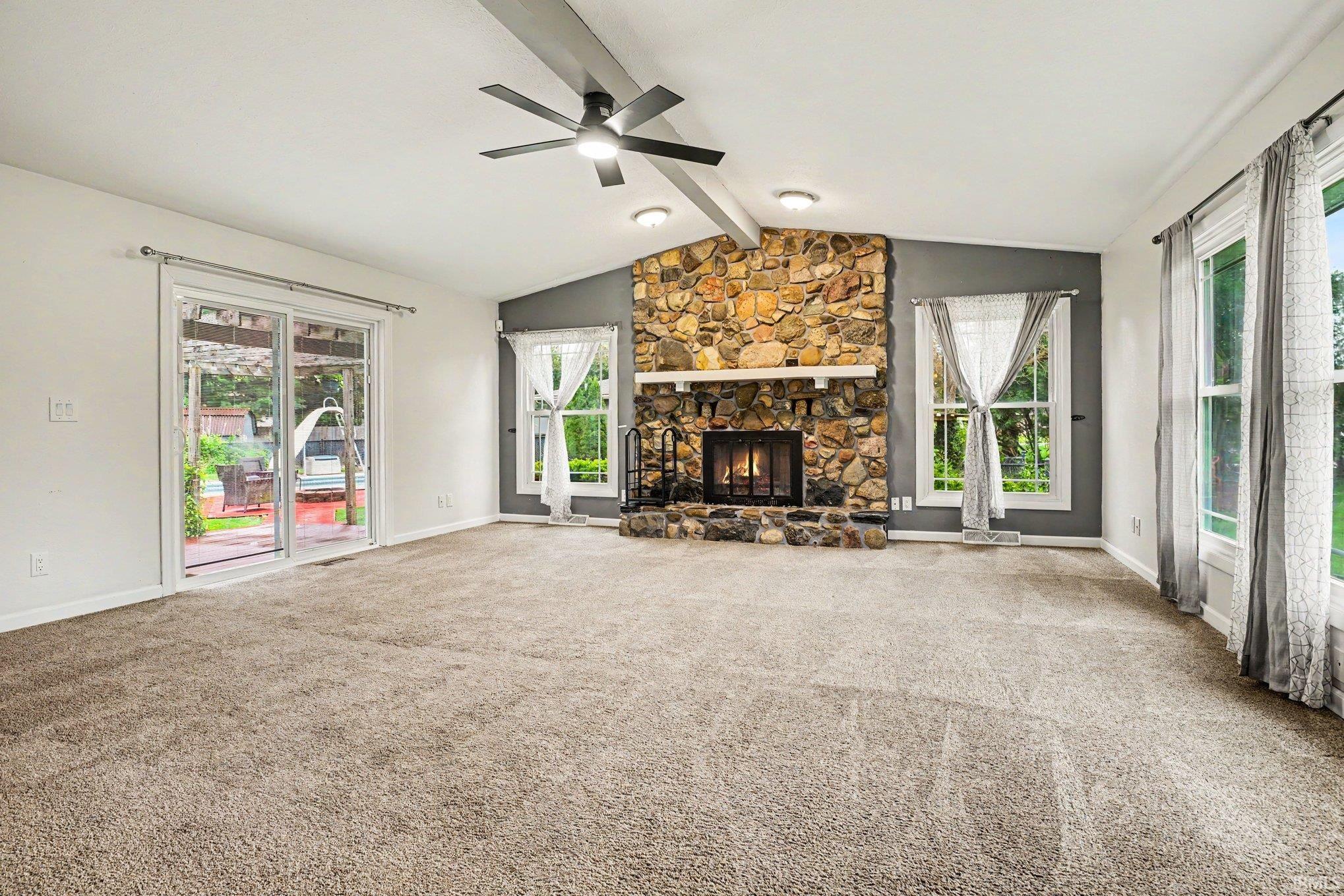 Spacious living area featuring a stone-faced fireplace with a mantel, vaulted ceiling with a ceiling fan, and large sliding glass doors providing access to the outdoors
