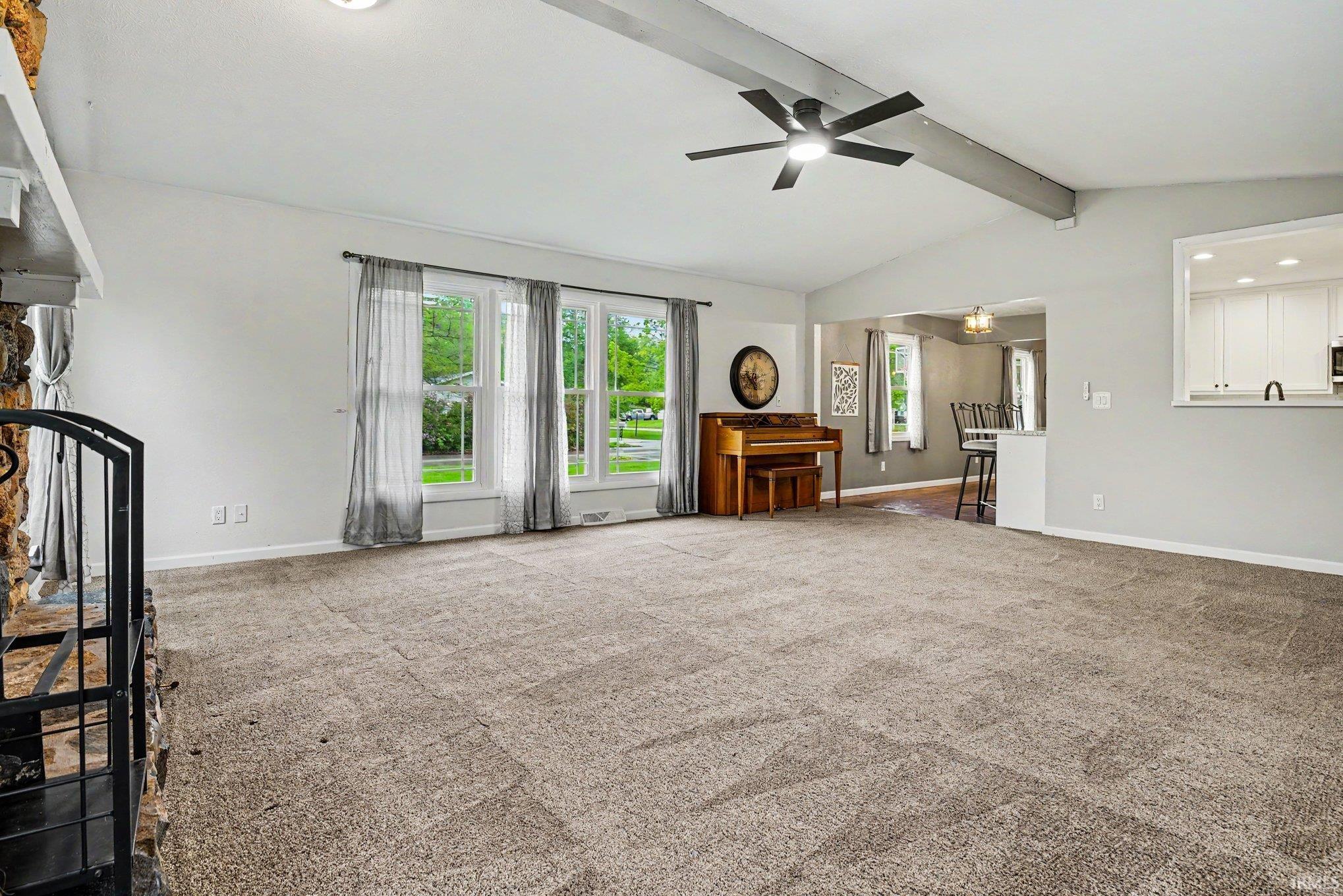 Spacious living area featuring vaulted ceilings with exposed beams, a ceiling fan, and large windows