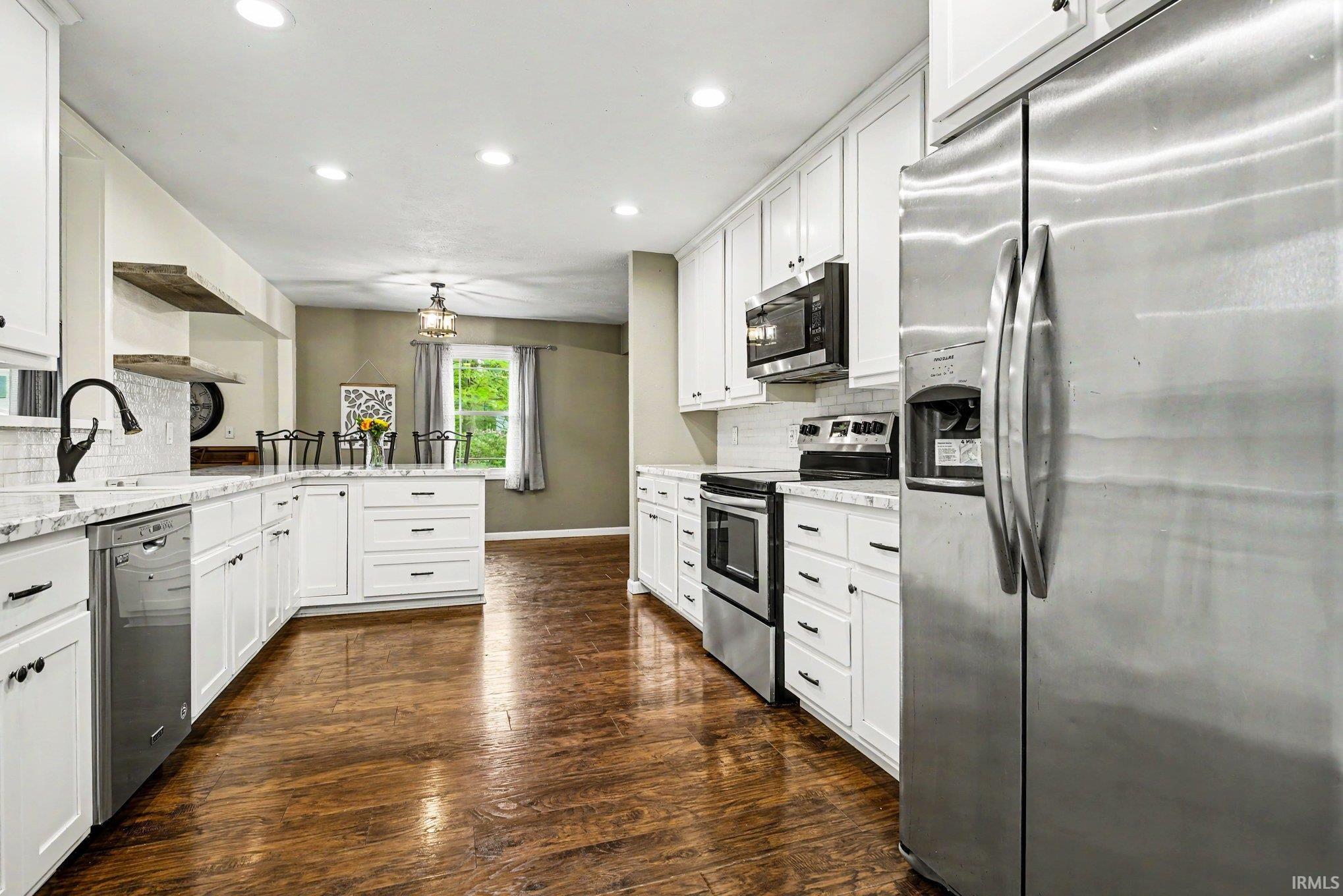 Kitchen featuring wood-finish flooring, white cabinetry with black hardware, stainless steel appliances, granite countertops, and recessed lighting