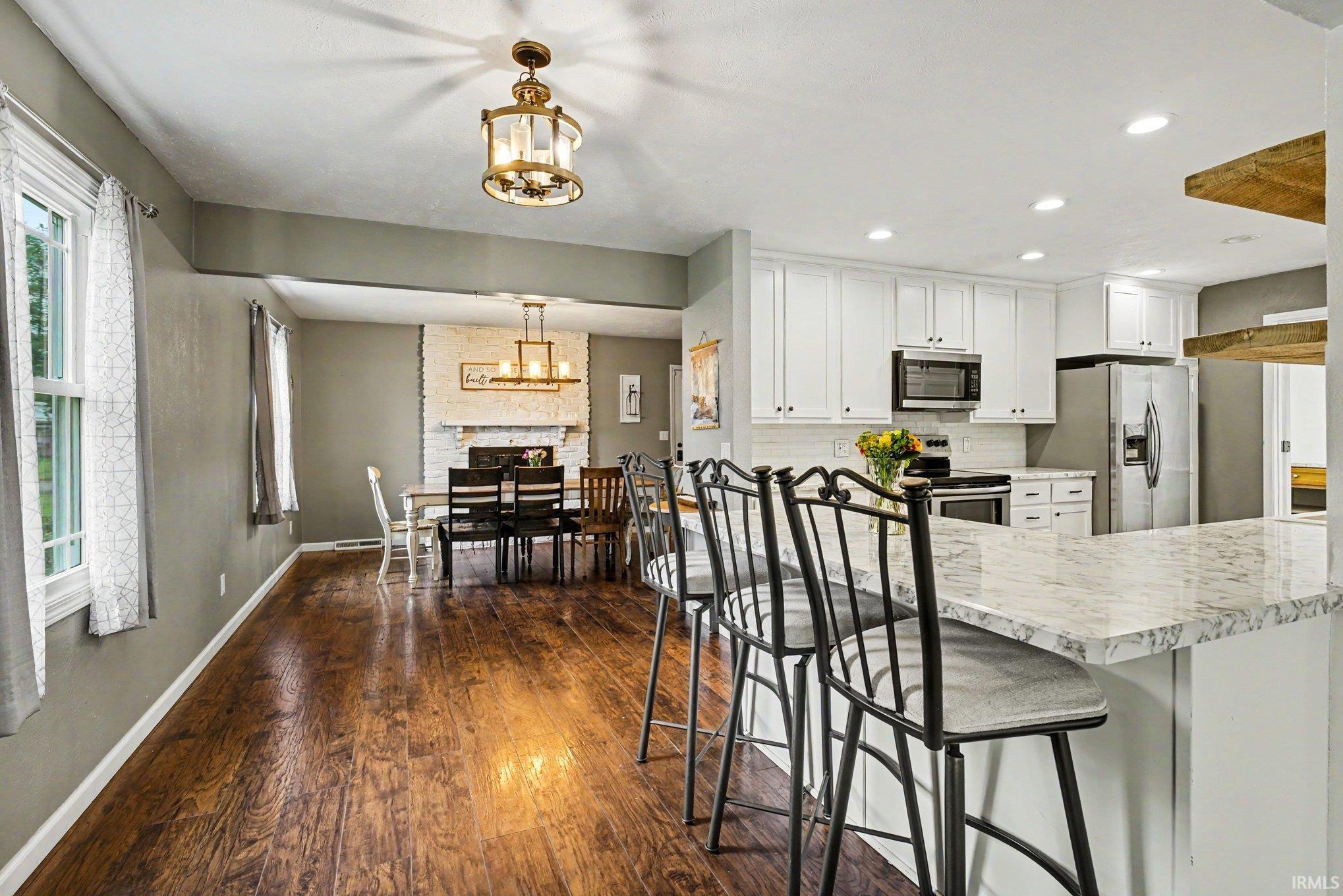 Open-concept kitchen and dining area featuring wood-finish flooring, white cabinetry, a stone-finish countertop, and stainless steel appliances