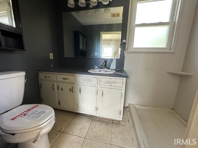Bathroom featuring a window, vanity with integrated sink, wall-mounted mirror, and tile flooring