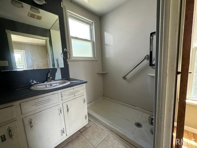 Bathroom featuring a vanity with a dark countertop and white cabinetry, a built-in shower stall with a grab bar, and a window providing natural light