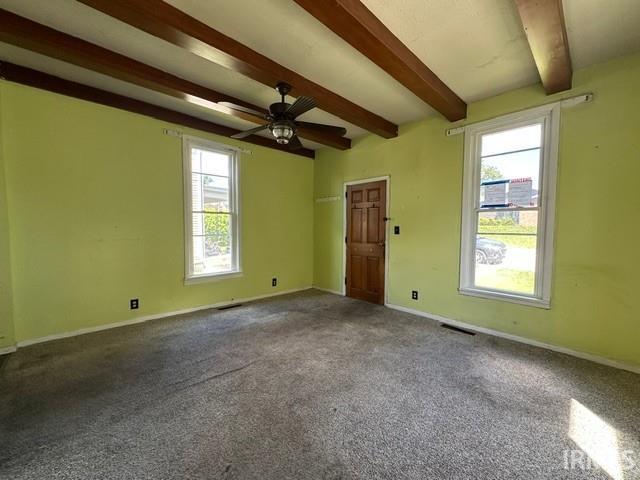 Room featuring exposed ceiling beams, two double-hung windows, a ceiling fan with light fixture, and a paneled wooden door