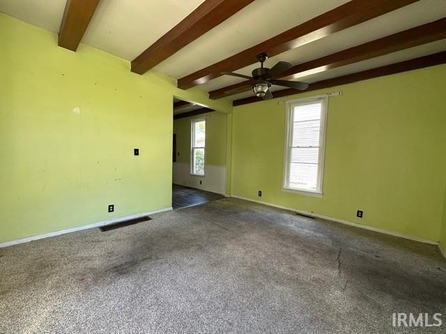 Spacious room featuring exposed wood-finish ceiling beams, a ceiling fan with integrated lighting, and multiple windows