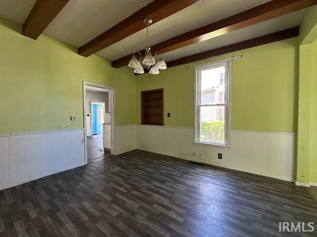 Spacious room featuring exposed ceiling beams, wood-finish flooring, and white wainscoting