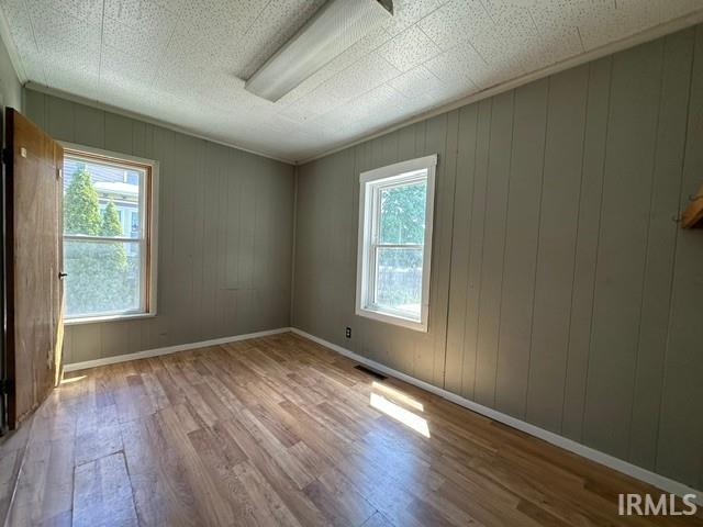 Room featuring wood-finish flooring, two windows, vertical paneling, and a drop ceiling with a fluorescent light fixture