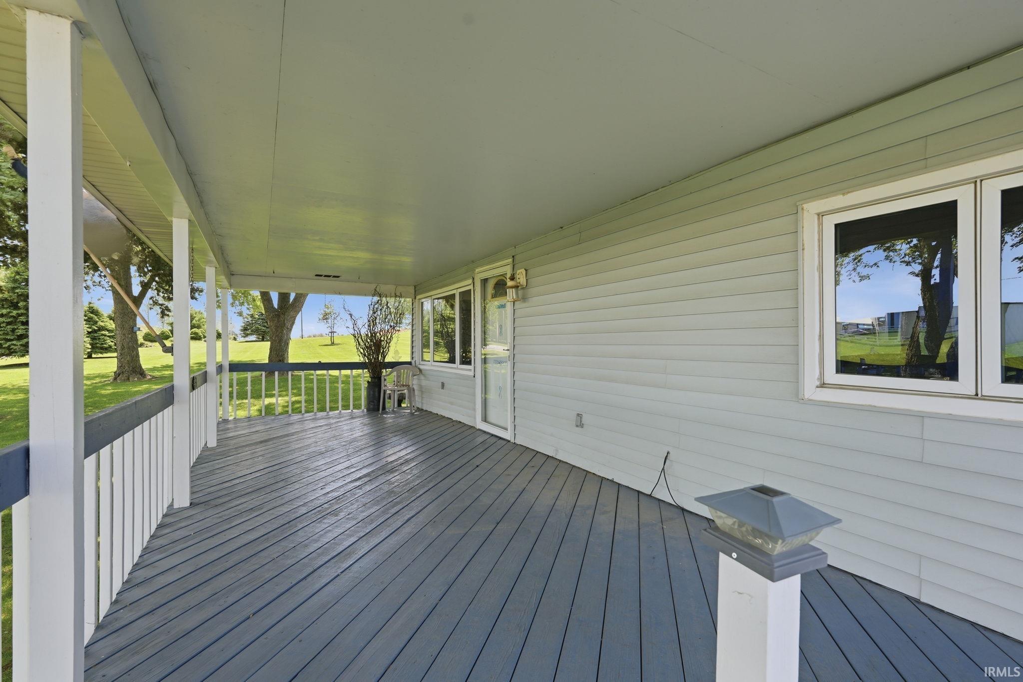 Covered porch with painted wood-finish flooring, white railing, light gray siding, and multiple windows