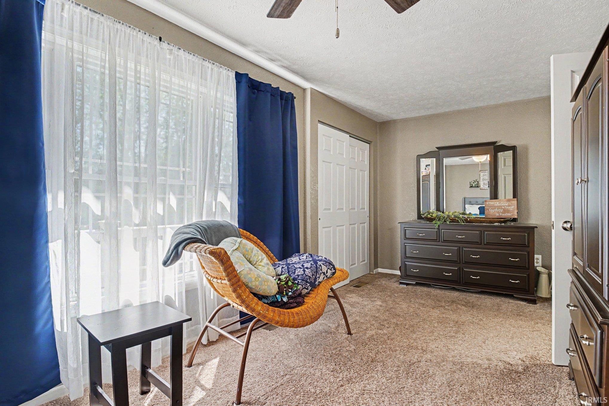 Carpeted interior space featuring a double window with blinds and sheer curtains, textured ceiling, bi-fold closet door, and a six-panel door