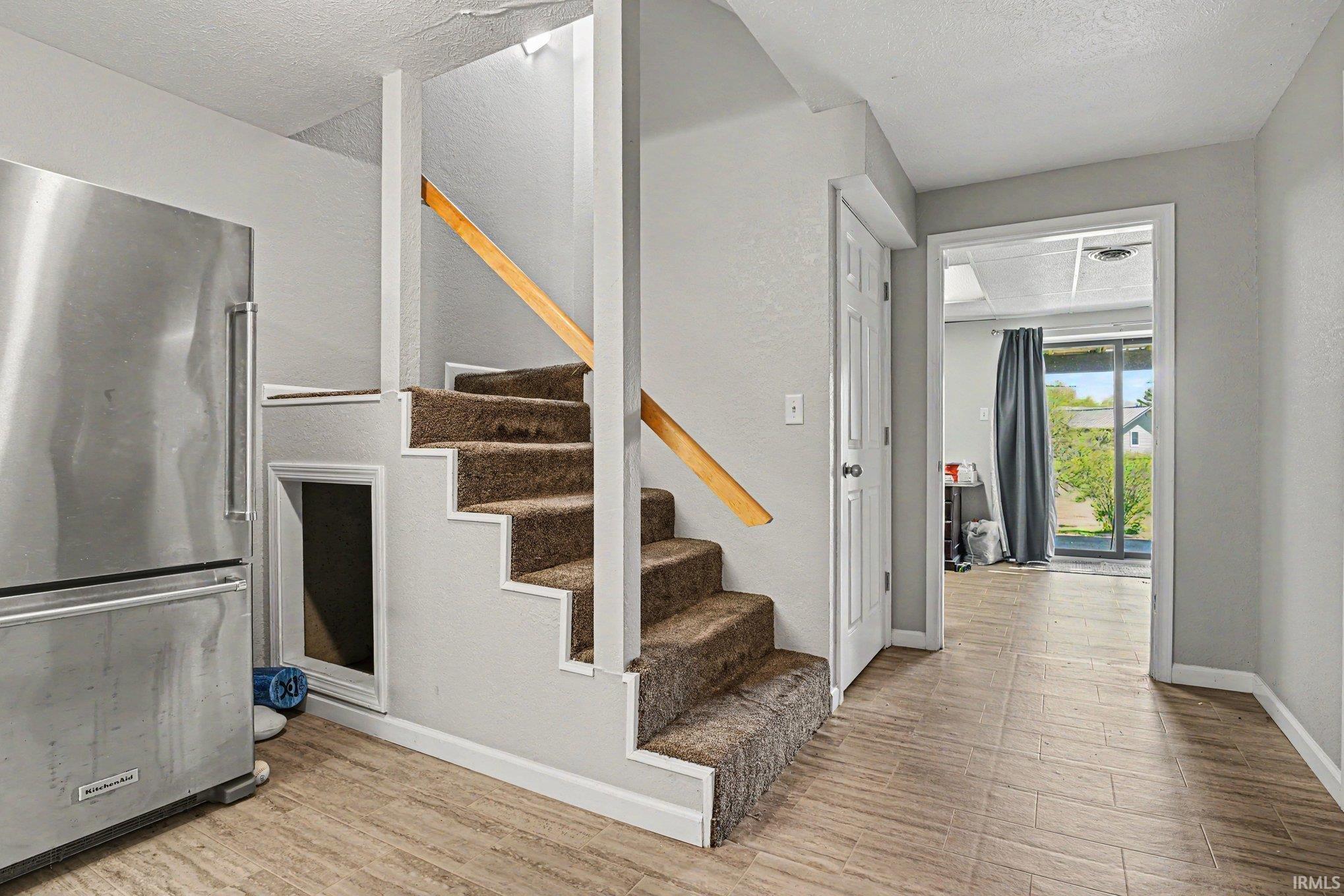 Carpeted staircase with wood-finish handrail, stainless steel refrigerator, tile-finish flooring, white paneled door, and a sliding glass door leading to the exterior