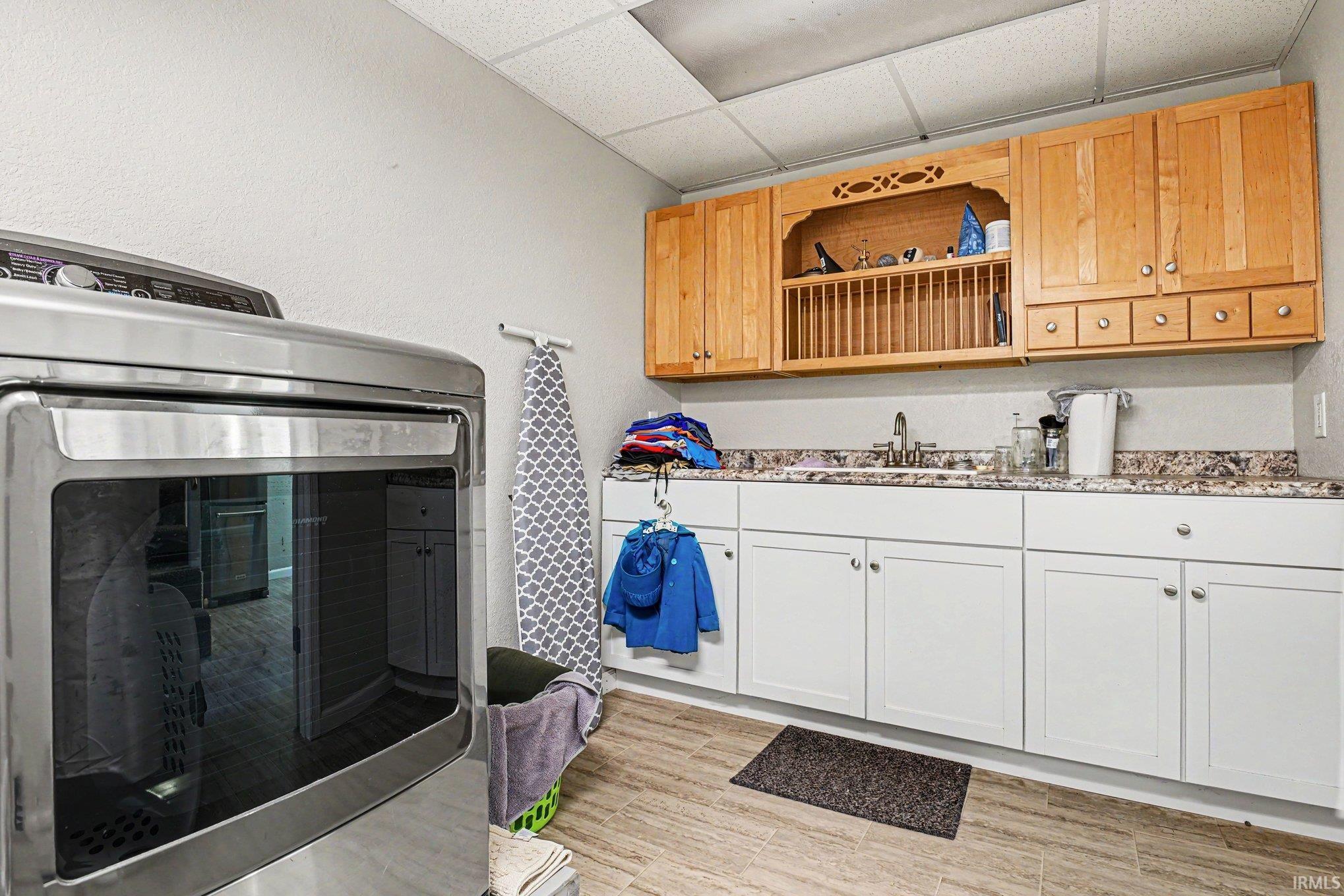 Utility room featuring wood-finish flooring, white lower cabinetry with a built-in sink, and light wood upper cabinetry with an integrated plate rack