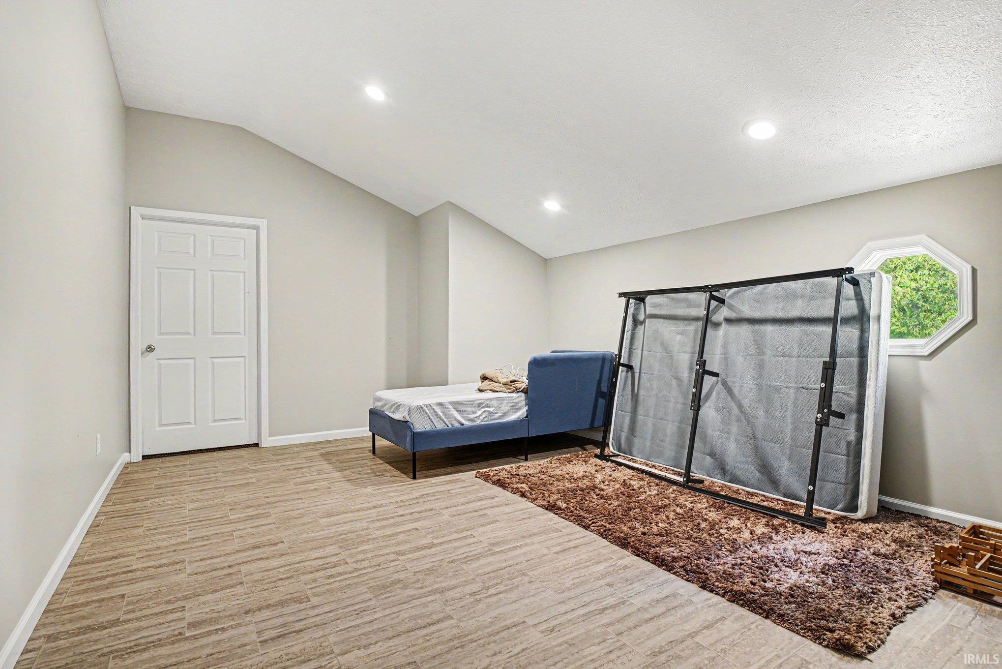Vaulted ceiling room featuring light-toned walls, wood-finish flooring, and recessed lighting