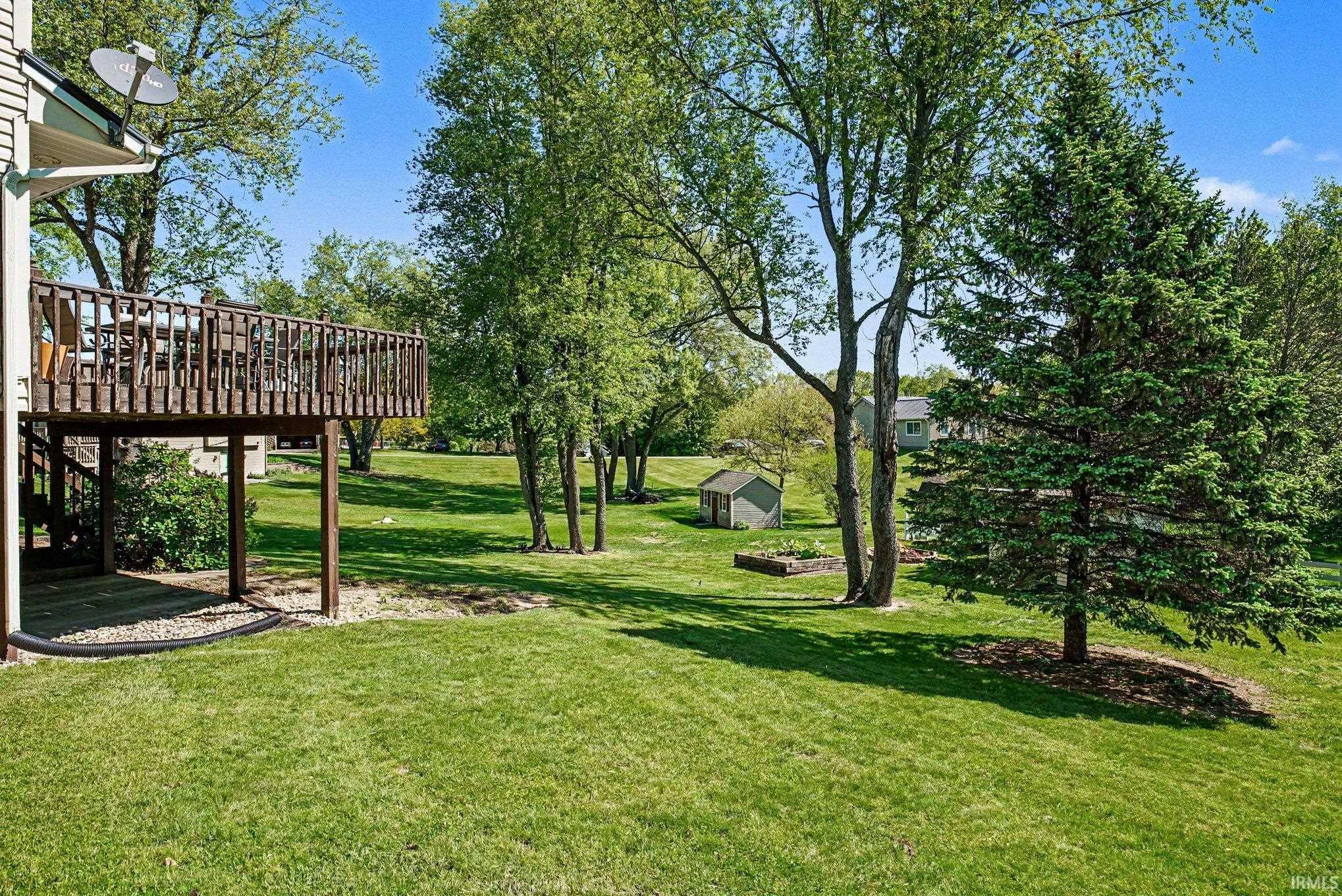 Expansive green lawn with mature trees and a raised wooden deck