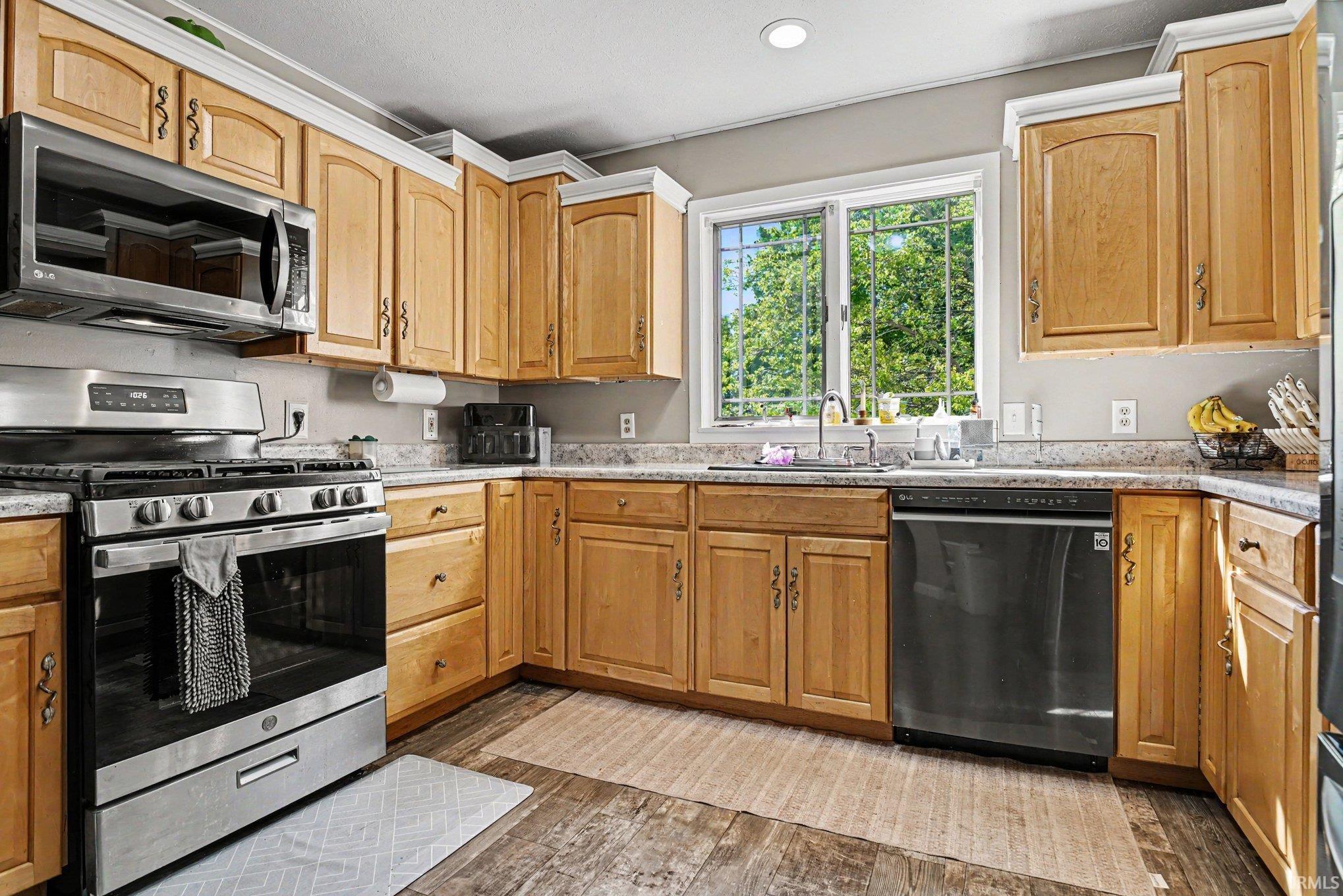 Kitchen featuring wood-finish cabinetry, stainless steel appliances, speckled countertops, and wood-finish flooring