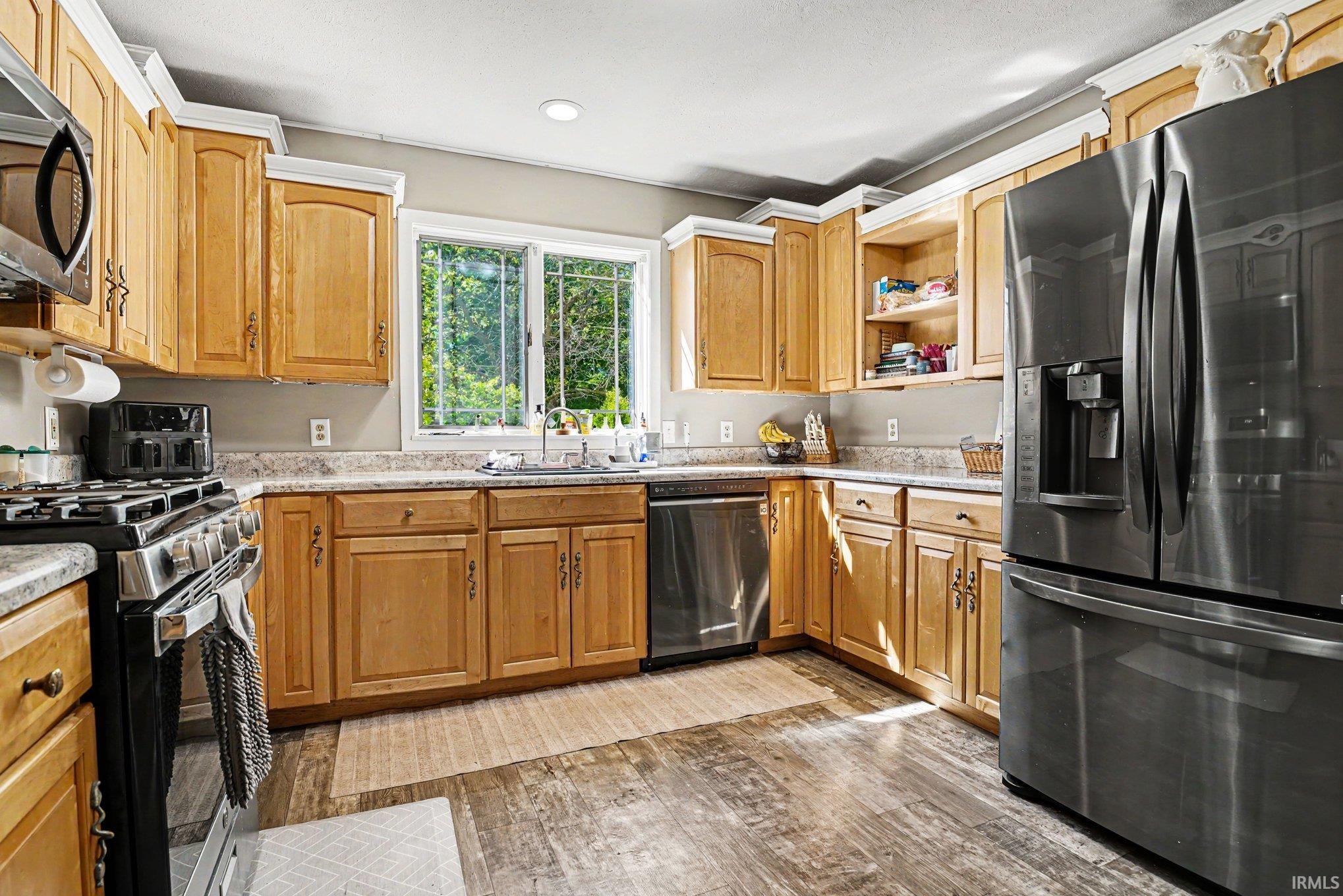 Kitchen featuring natural wood cabinetry, stainless steel appliances, a double window above the sink, wood-finish flooring, and light-toned countertops
