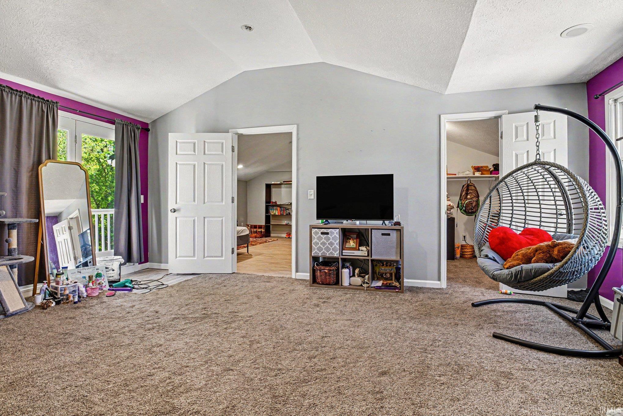 Spacious room featuring vaulted ceilings, plush carpet flooring, and double French doors opening to an exterior balcony