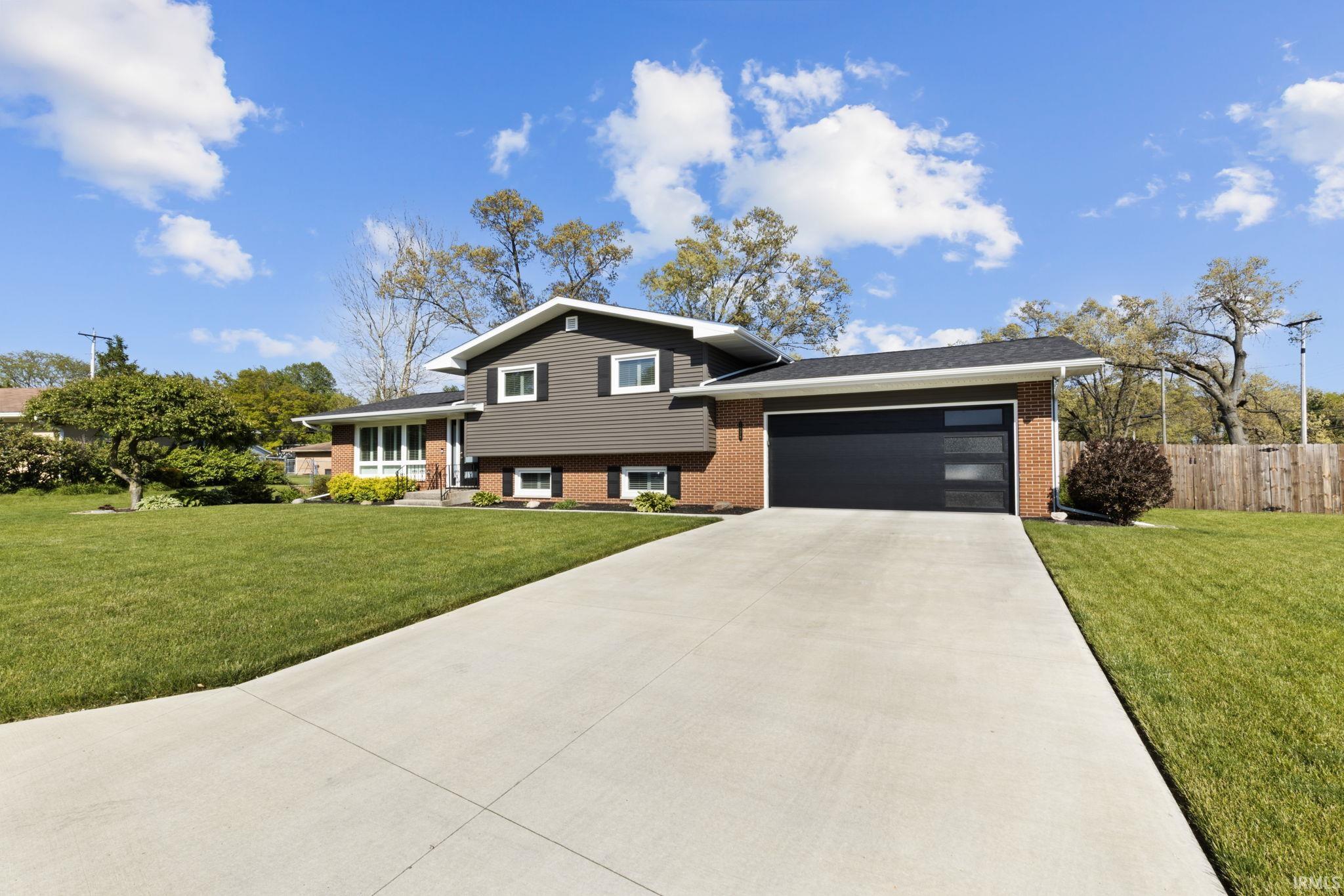 Split-level residence featuring a brick and horizontal siding exterior, a contemporary garage door with frosted glass panels, and a concrete driveway