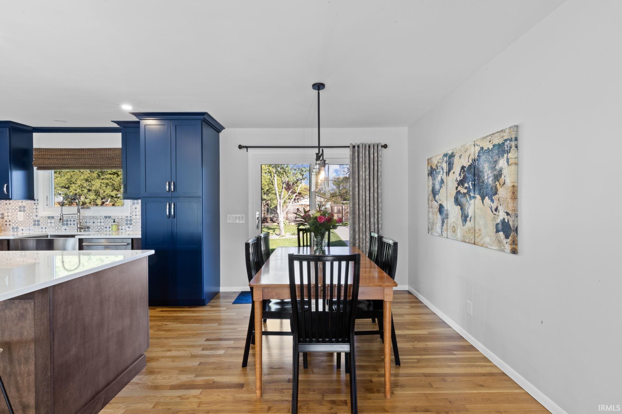 Open-concept kitchen and dining area featuring wood-finish flooring, white countertops, blue cabinetry, and a glass-paned exterior door