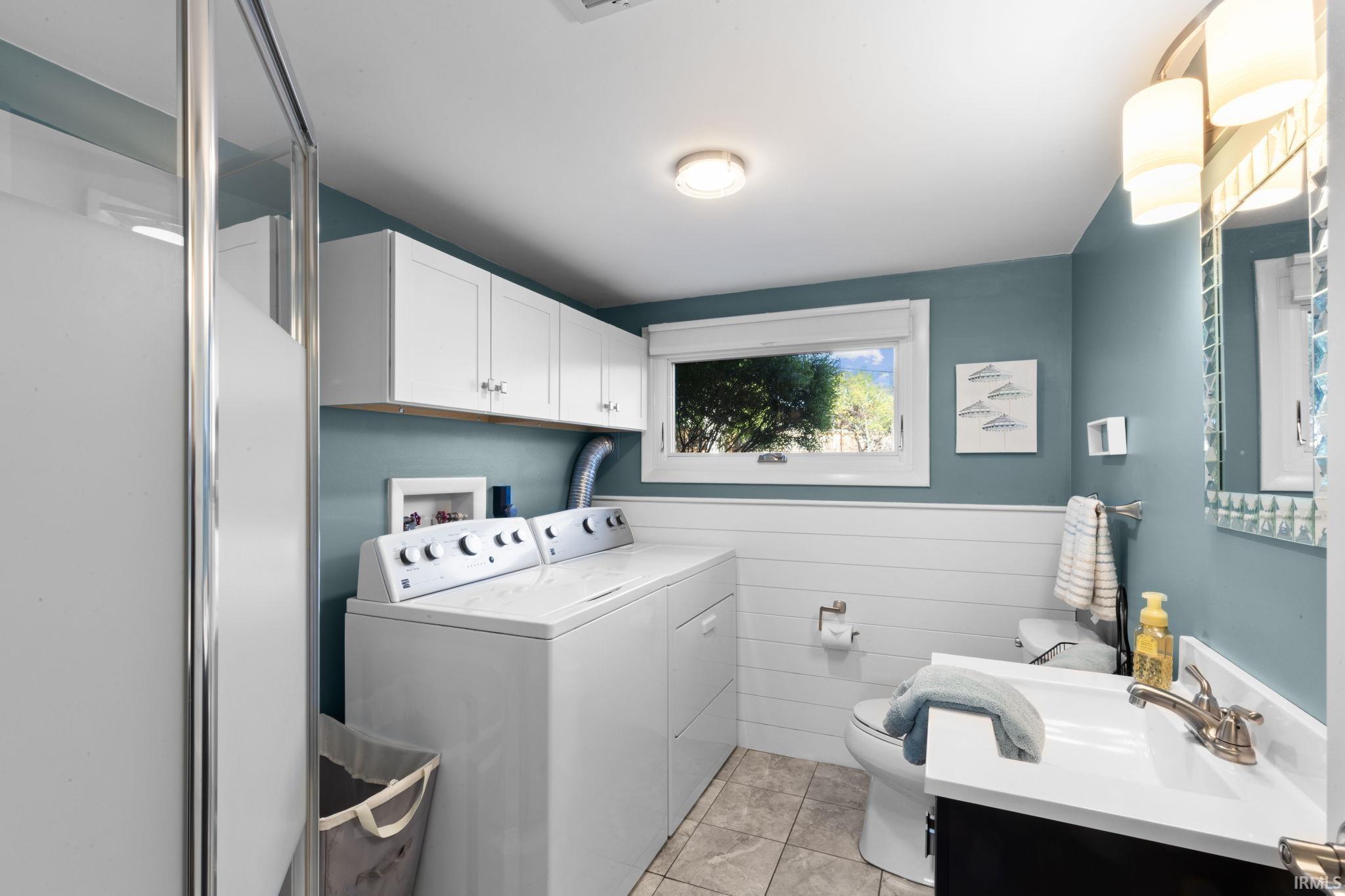 Bathroom featuring a shower enclosure, integrated laundry appliances, wall-mounted cabinetry, a single window, and a vanity with a sink