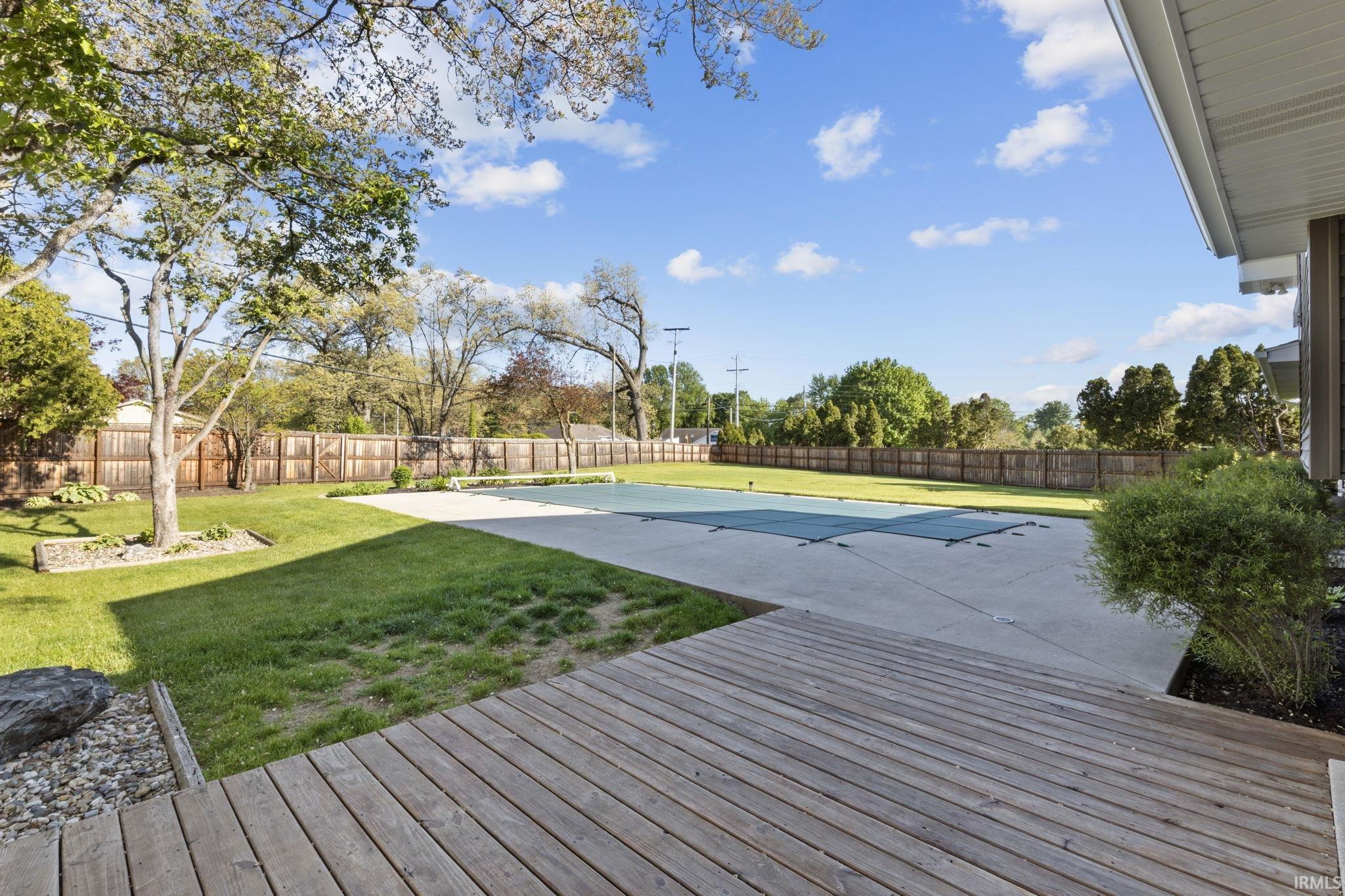 Expansive backyard featuring a covered pool, concrete patio, and a spacious wood deck