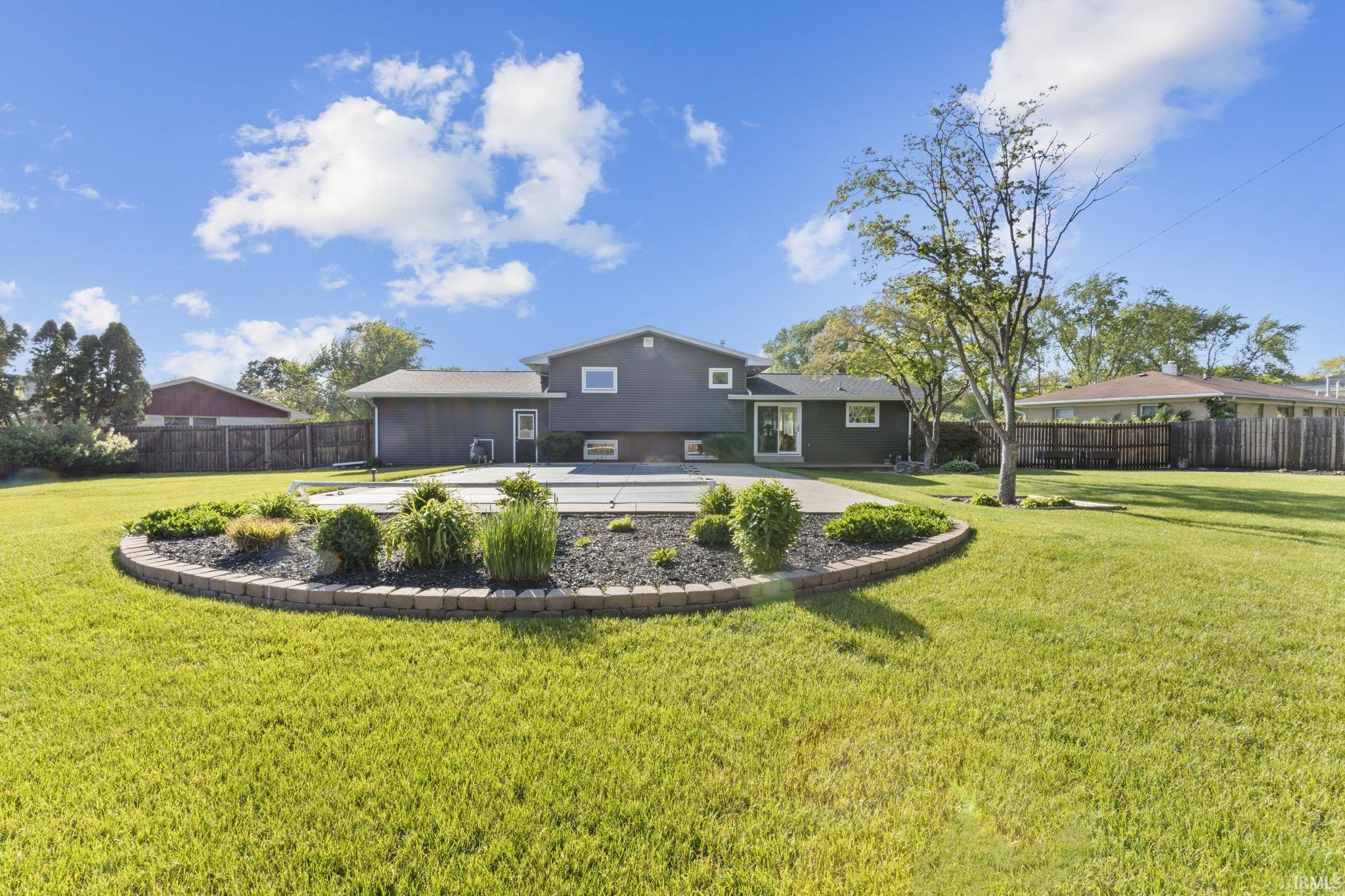 Expansive backyard featuring a manicured lawn, a swimming pool with a cover, and a rounded garden bed with brick-paver edging