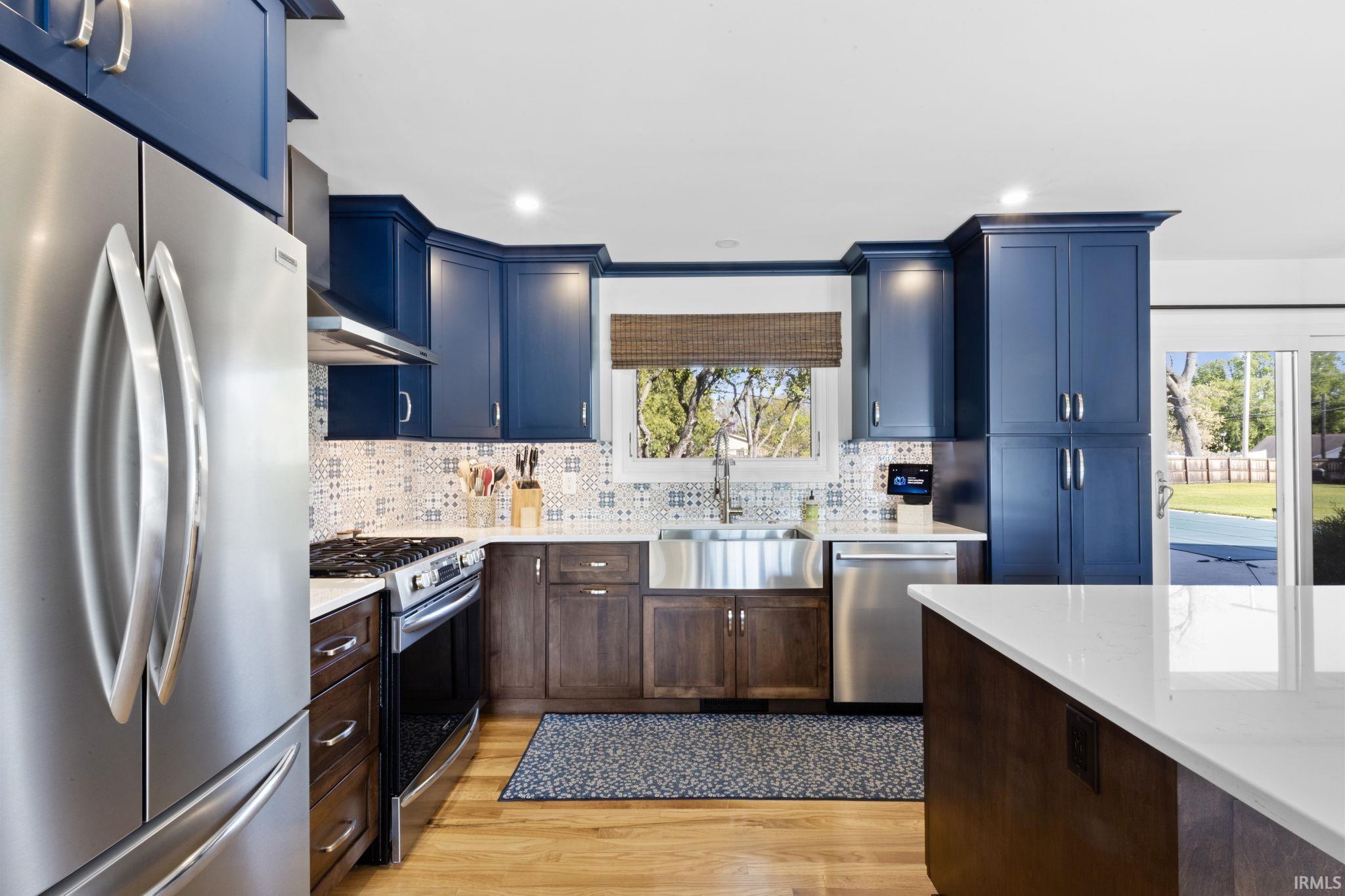 Modern kitchen featuring two-tone cabinetry, stainless steel appliances, a farmhouse sink, decorative tile backsplash, and light wood-finish flooring