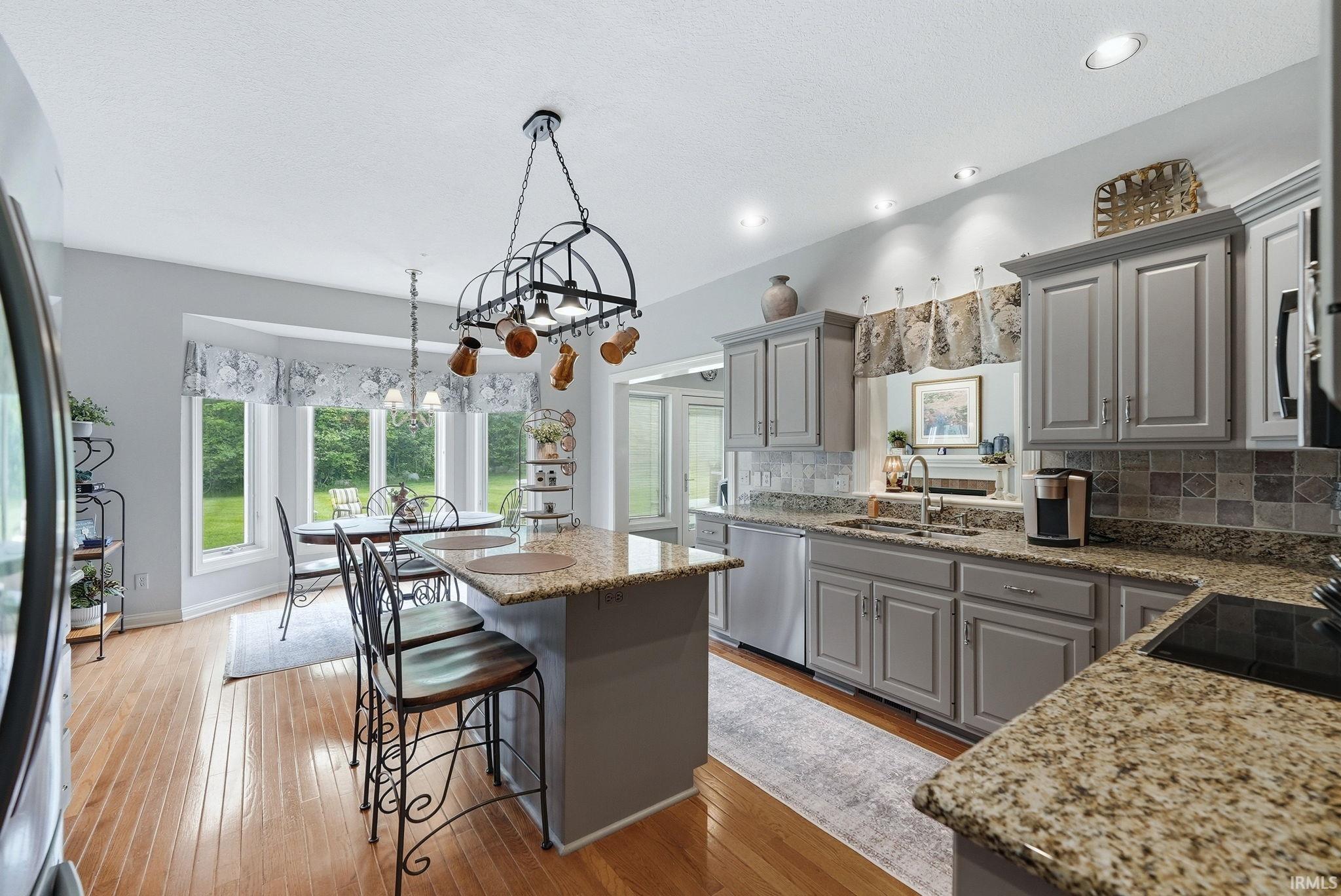 Kitchen featuring gray cabinetry, granite countertops, tile backsplash, stainless steel appliances, and wood-finish flooring