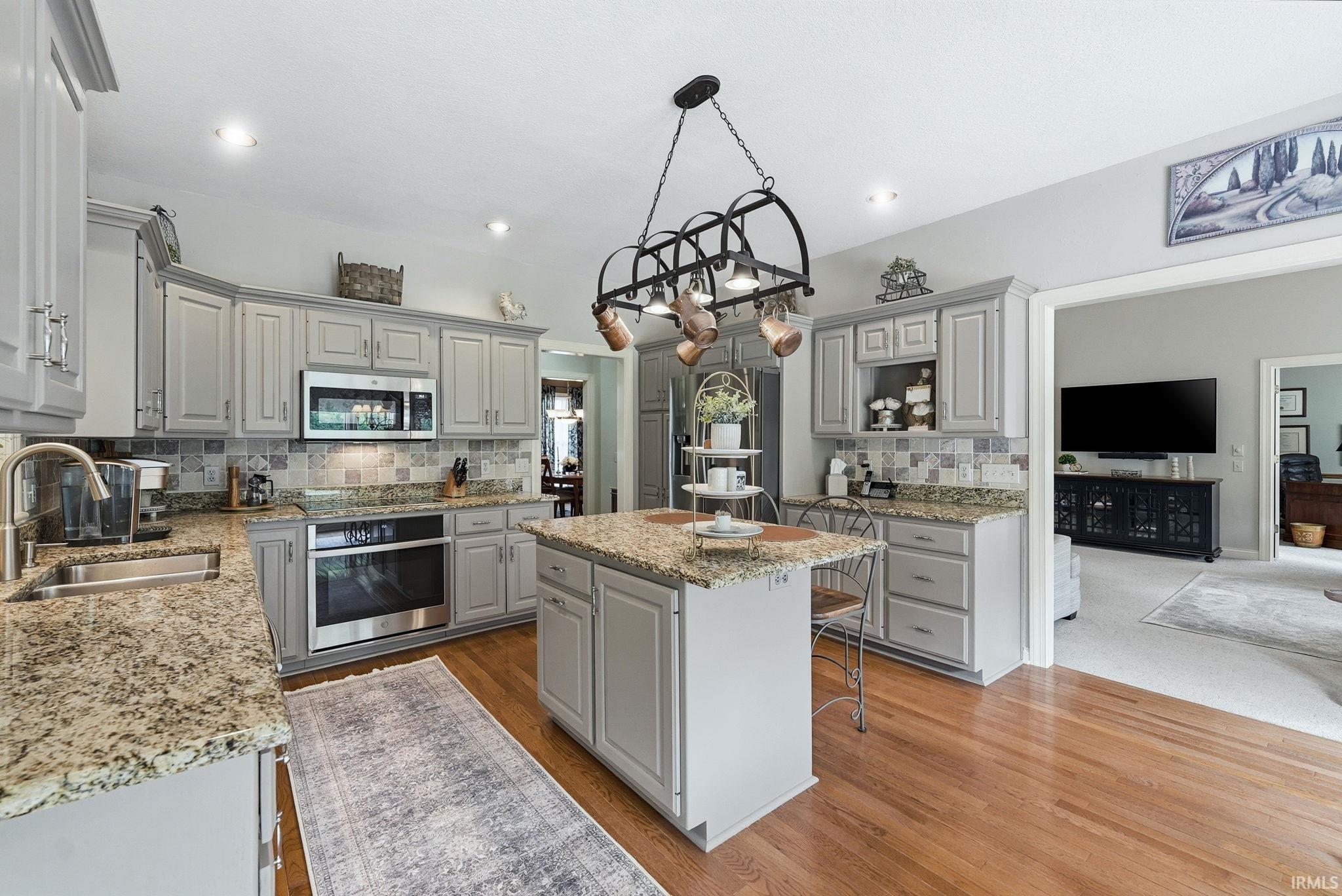 Spacious kitchen featuring hardwood flooring, light gray cabinetry, granite countertops, and stainless steel appliances, including a built-in oven and microwave