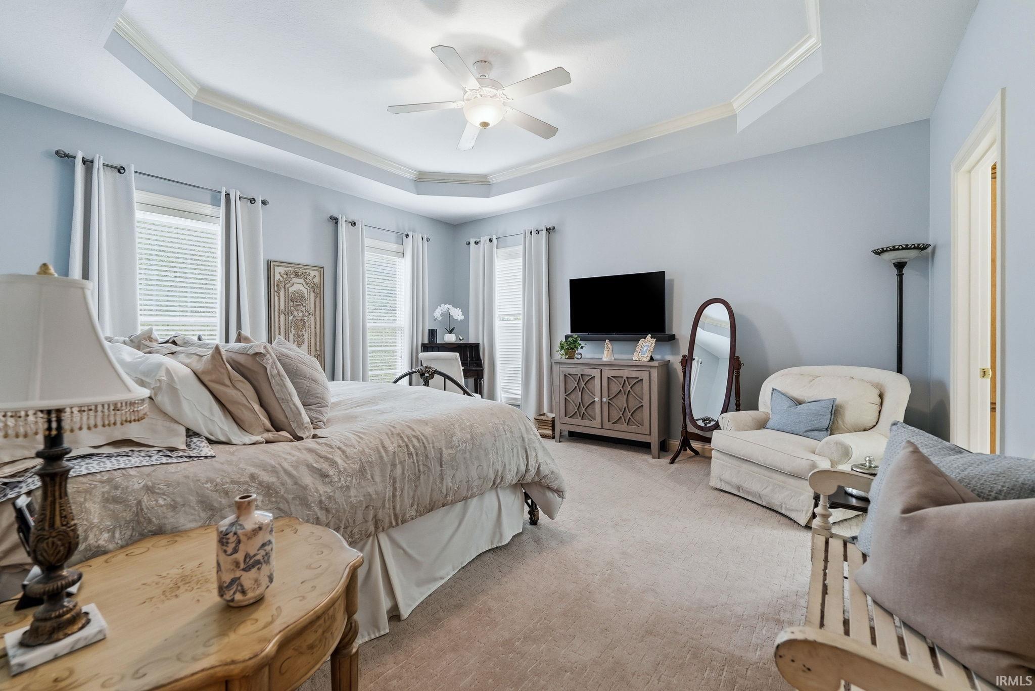 Spacious bedroom featuring light blue walls and a tray ceiling with crown molding