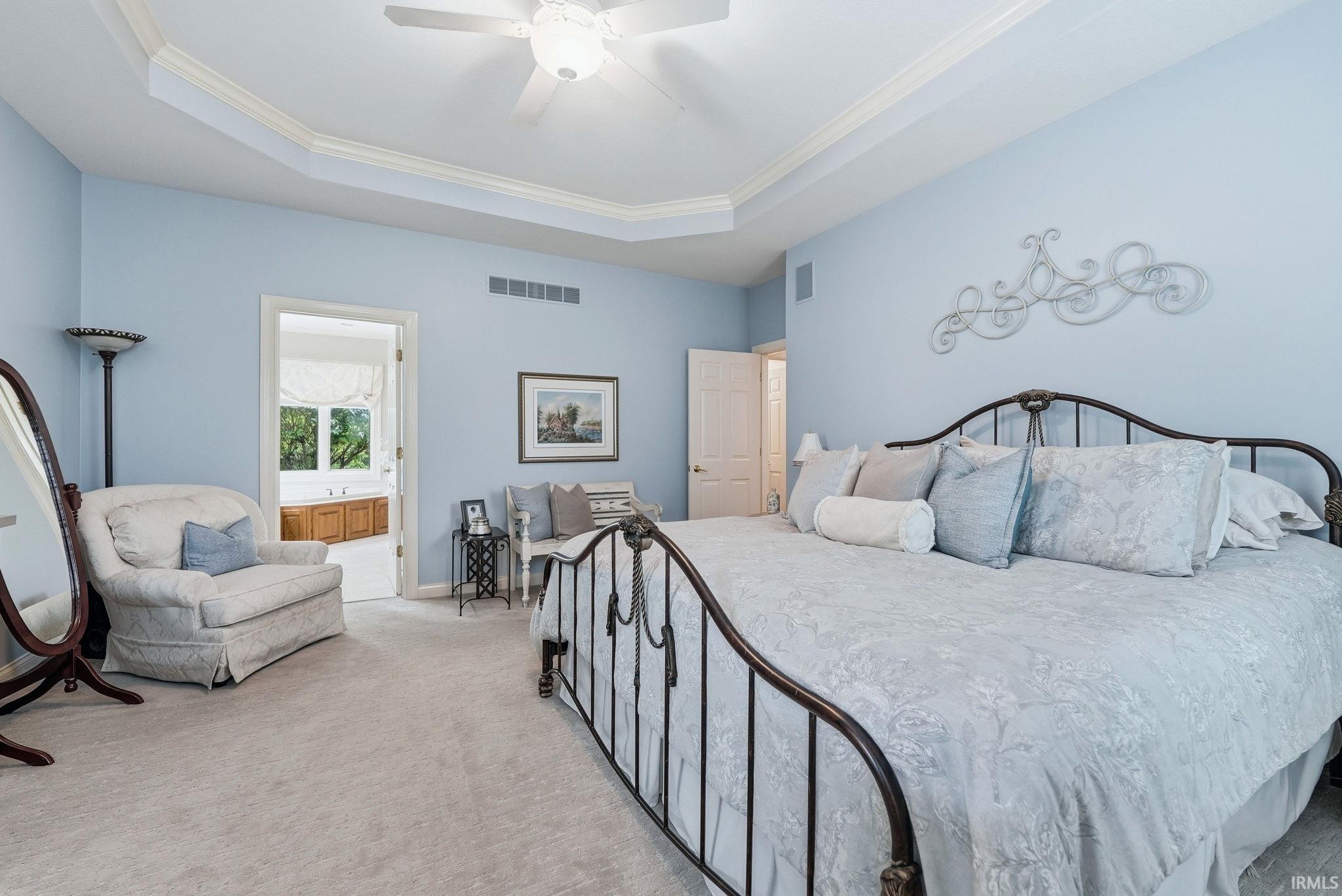 Spacious main floor bedroom en-suite featuring a tray ceiling with crown molding and a ceiling fan.
