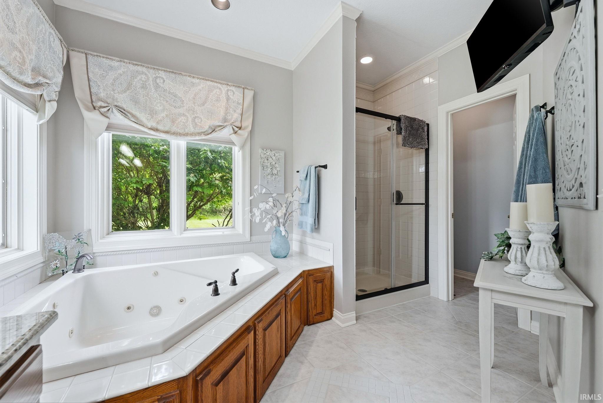 Corner soaking tub with tile surround, wood cabinetry, and multiple windows