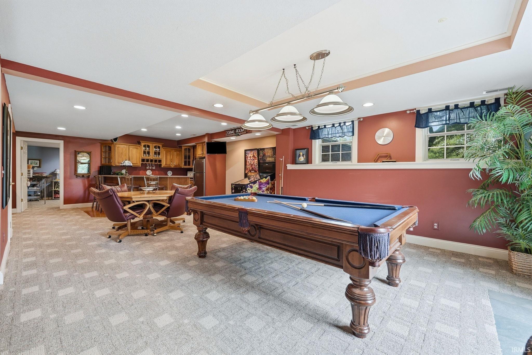 Spacious recreational room featuring patterned carpeting, recessed lighting, and a built-in wet bar with wood cabinetry