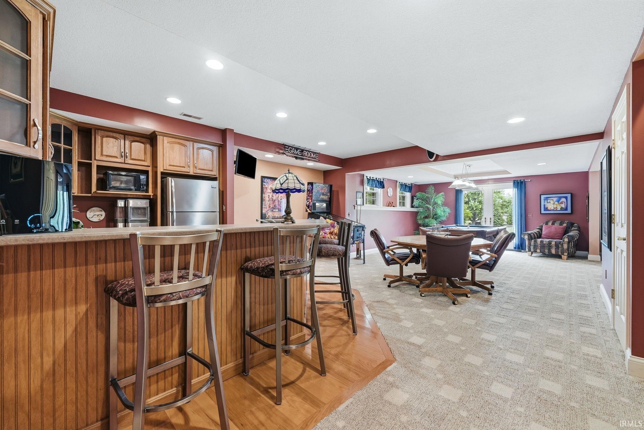 Lower-level entertainment space featuring a built-in bar with wood-finish cabinetry, stainless steel refrigerator, and recessed lighting