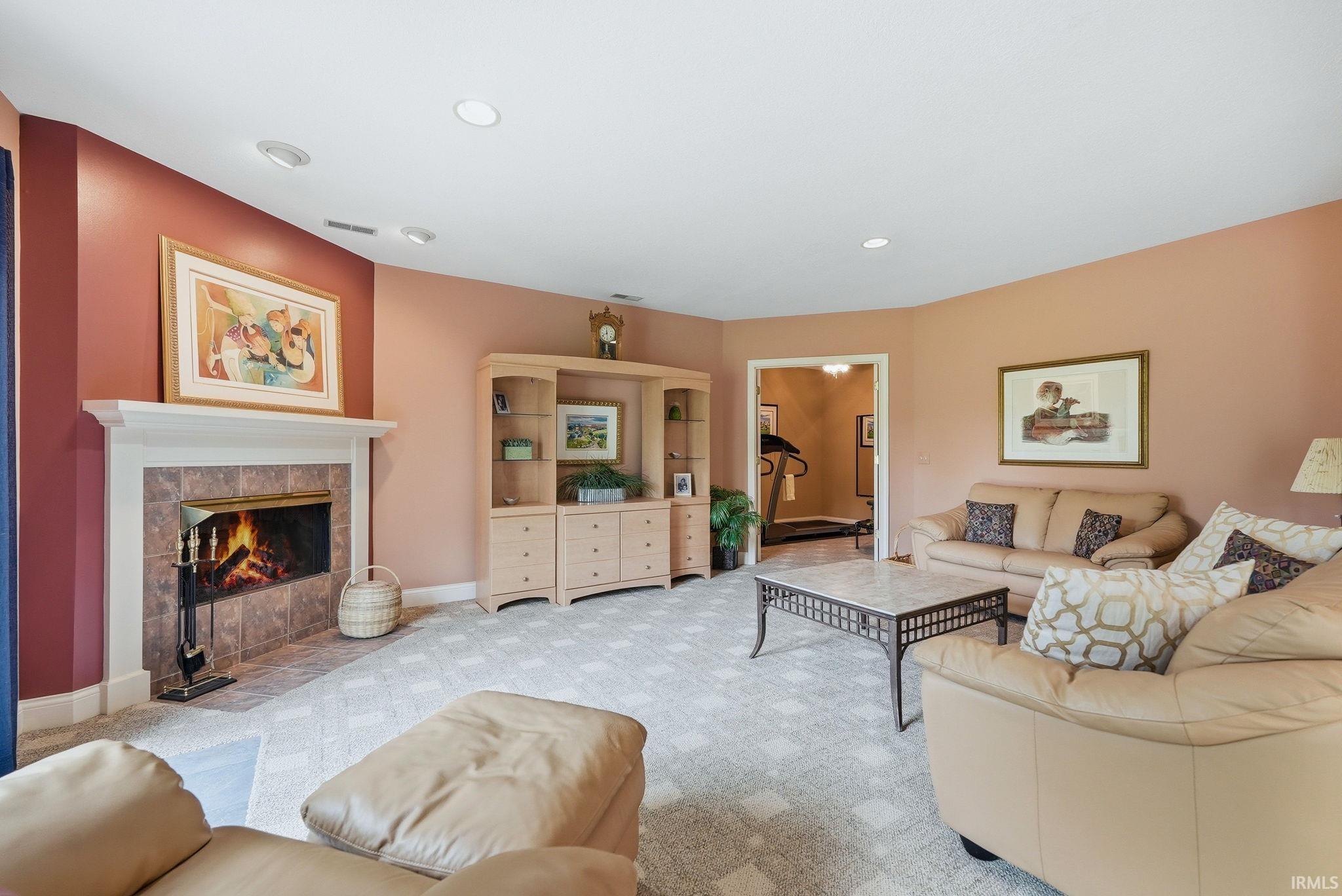 Recessed lighting illuminates this living space featuring a fireplace with a white mantel and tile surround, light-colored carpeting, and a built-in media cabinet