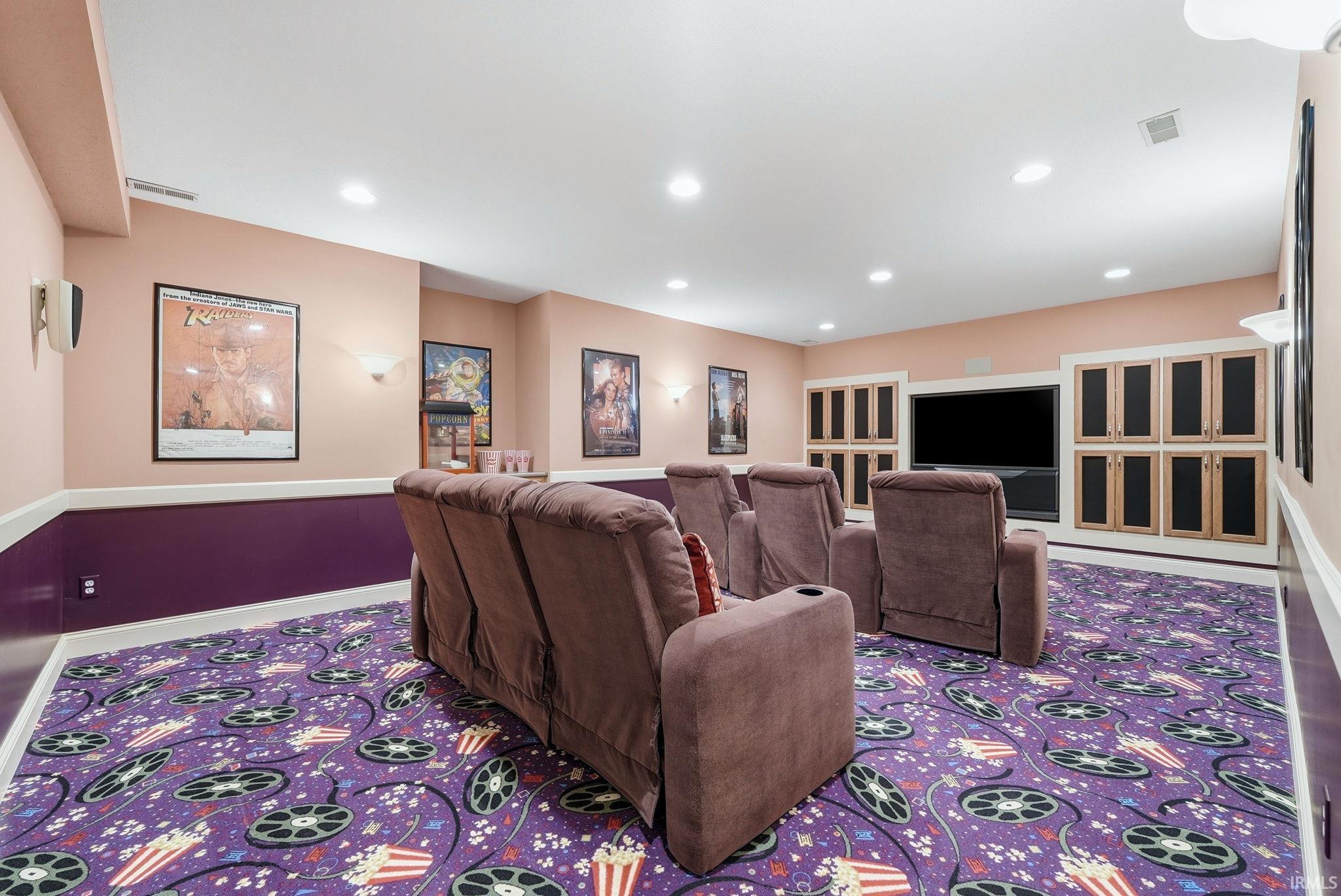 Media room featuring a recessed television screen, built-in cabinetry, recessed lighting, wall sconces, and colorful patterned carpeting