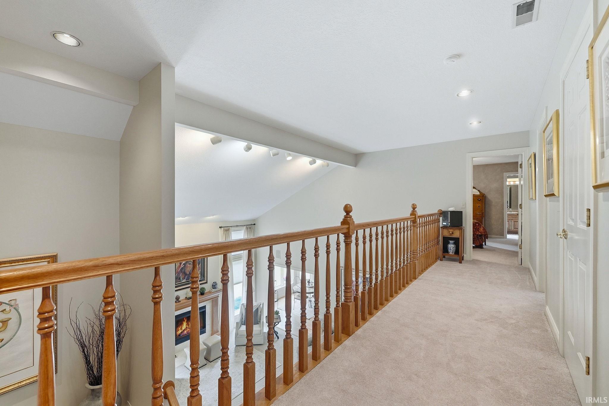 Upper-level hallway featuring a wooden balustrade overlooking a lower living space with a fireplace