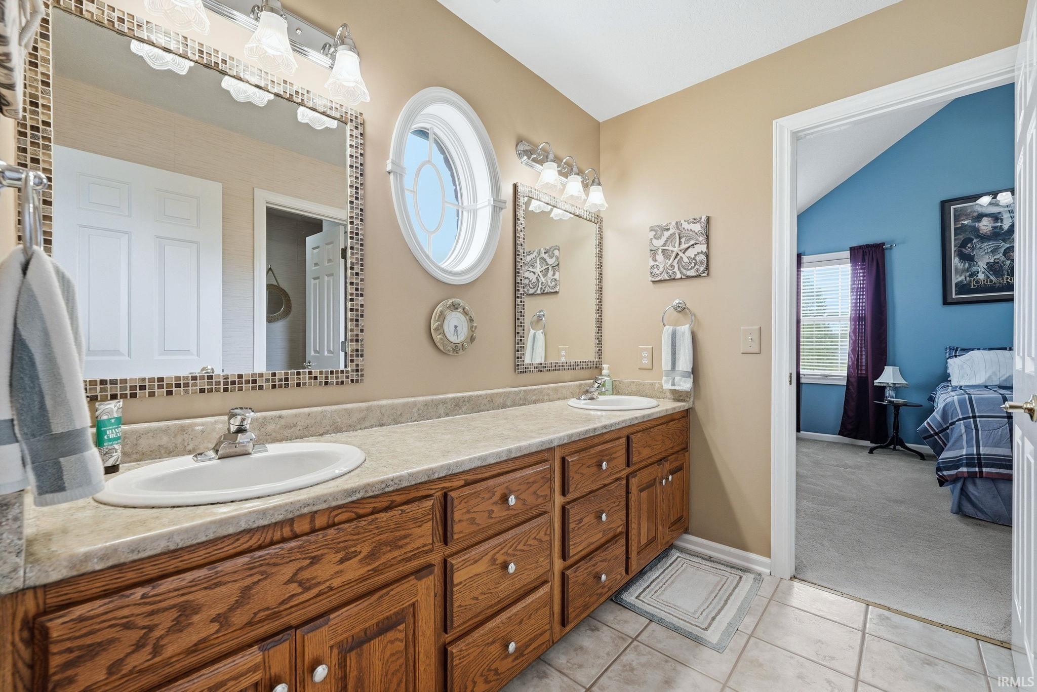 Dual vanity with wood-finish cabinetry, neutral countertops, and tile flooring