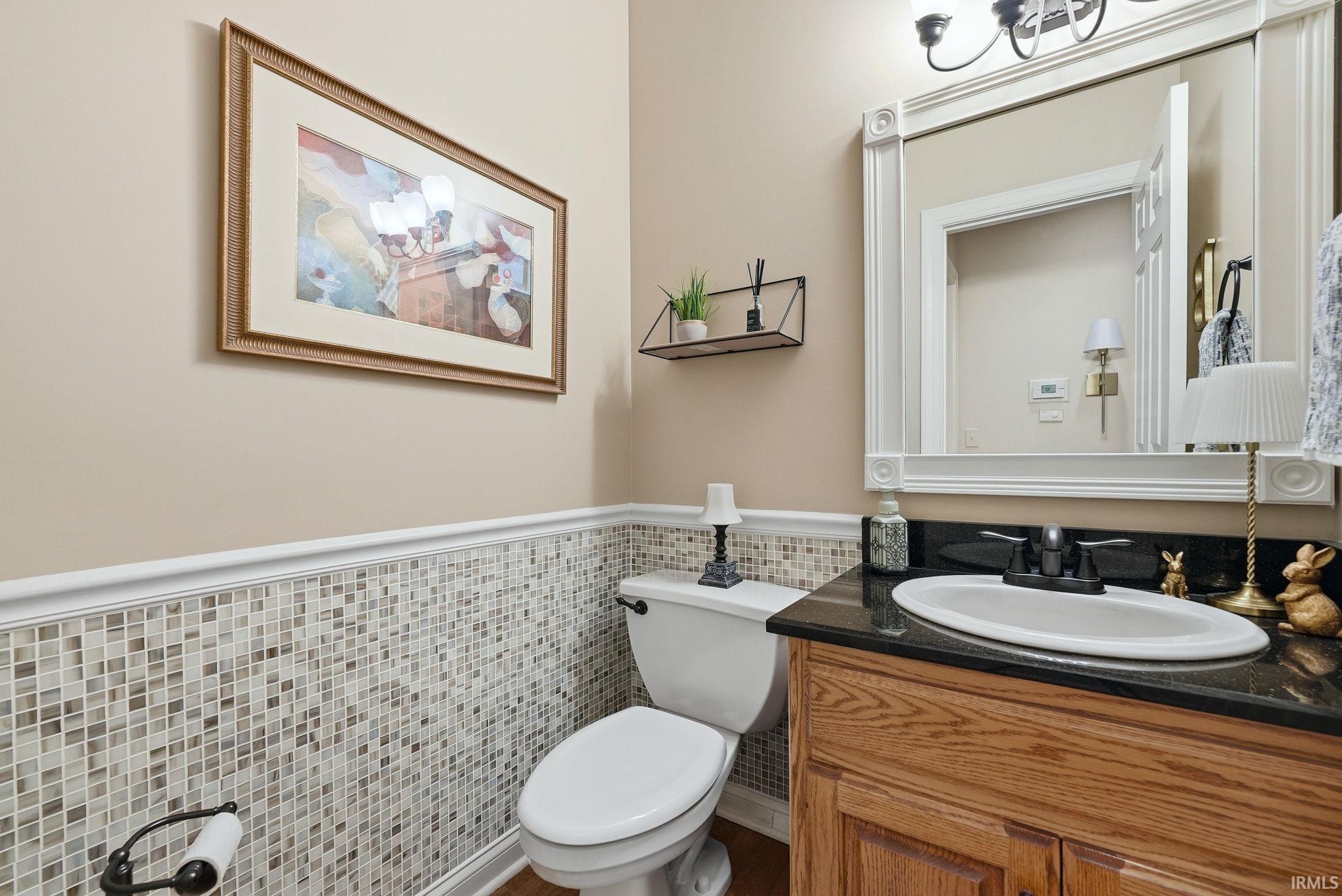 Bathroom featuring a wood-finish vanity with a black countertop and oval sink, mosaic tile wainscoting, and a decorative framed mirror