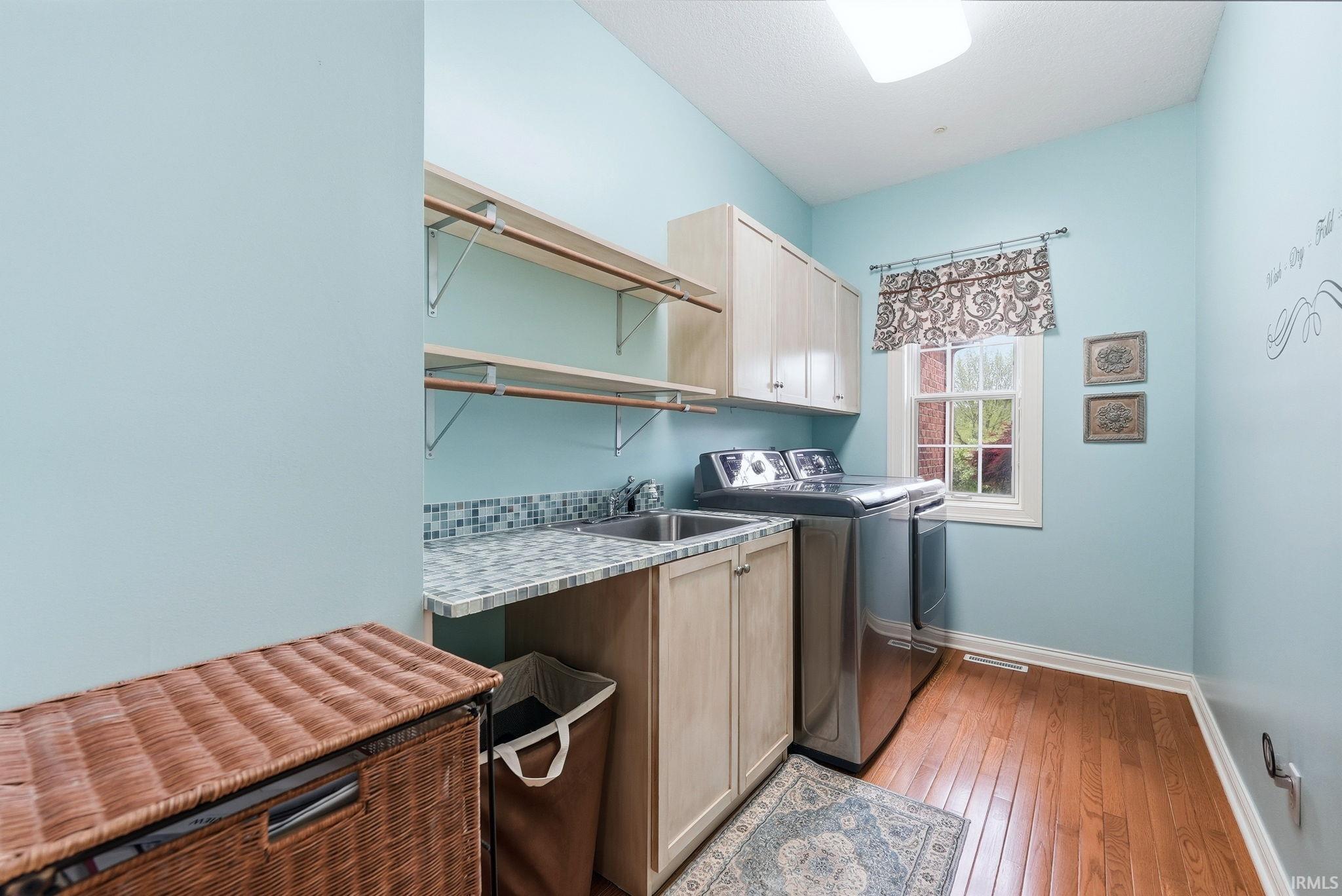 Laundry room featuring wood-finish flooring, light cabinetry, a built-in sink, upper shelving, and a window