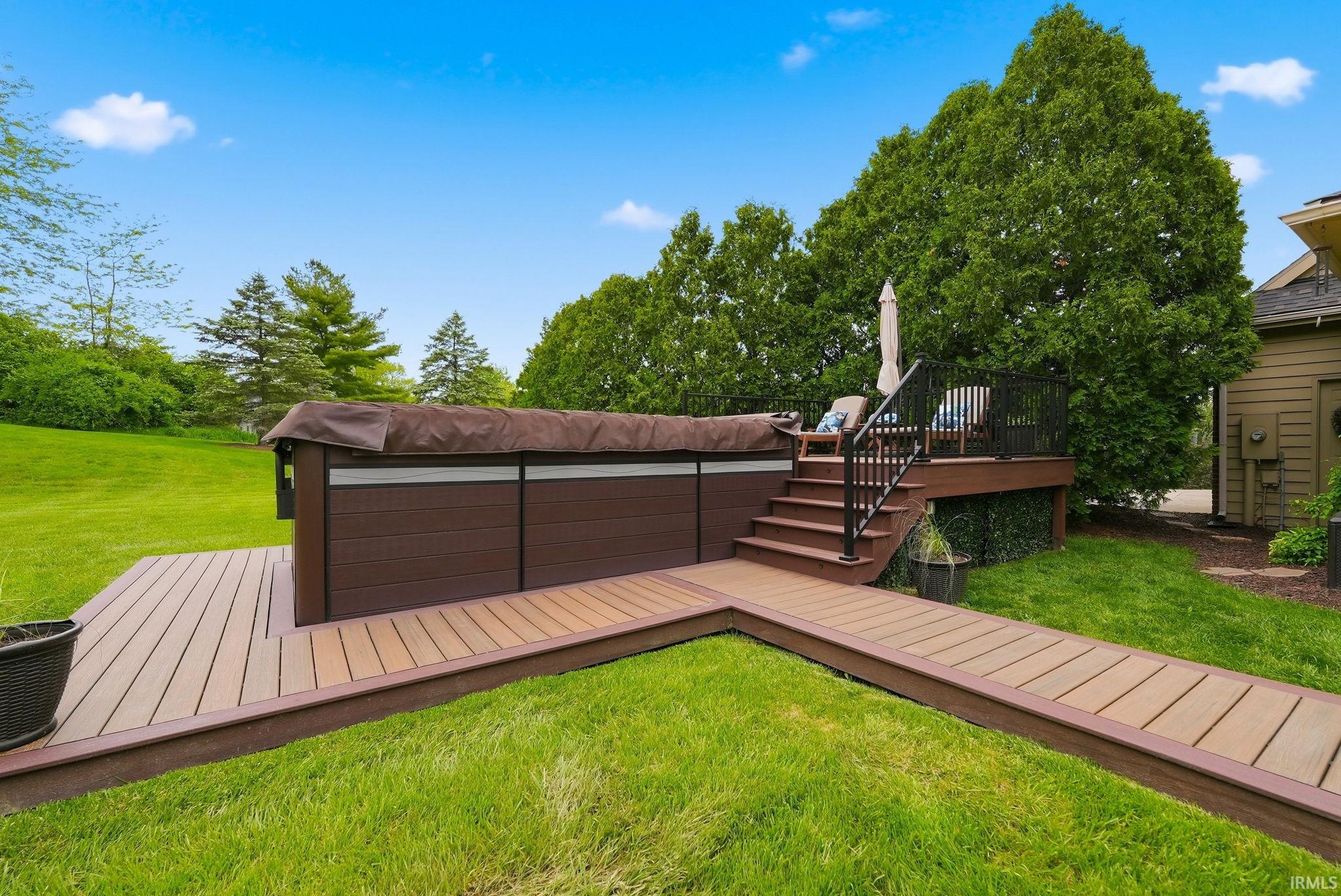 Spacious outdoor area featuring a hot tub, composite decking, and mature landscaping