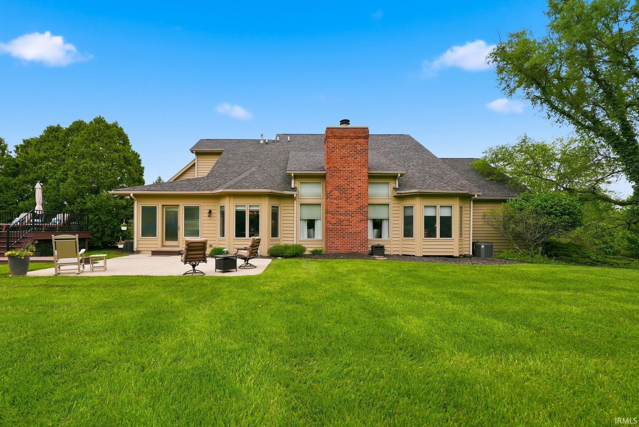 Spacious green lawn surrounding a beige-sided residence with a dark shingle roof
