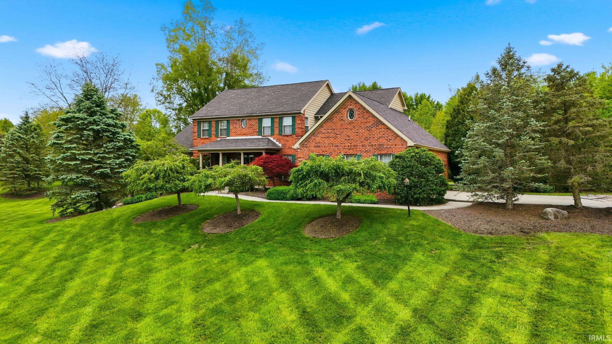 Brick-front residence featuring a covered front porch, gabled rooflines, and evergreen landscaping