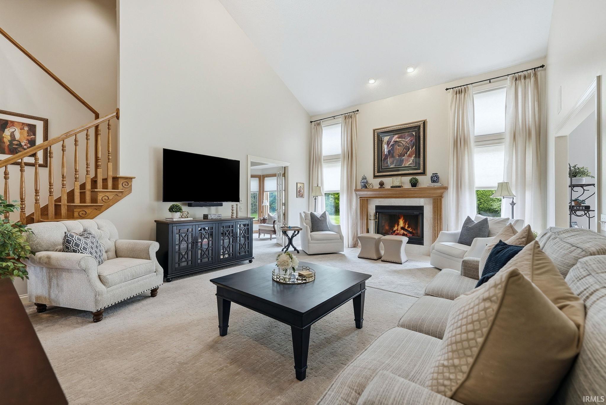 Vaulted ceiling living room featuring a recessed fireplace with a wood mantle, carpeted flooring, a staircase with wood banister, and large windows