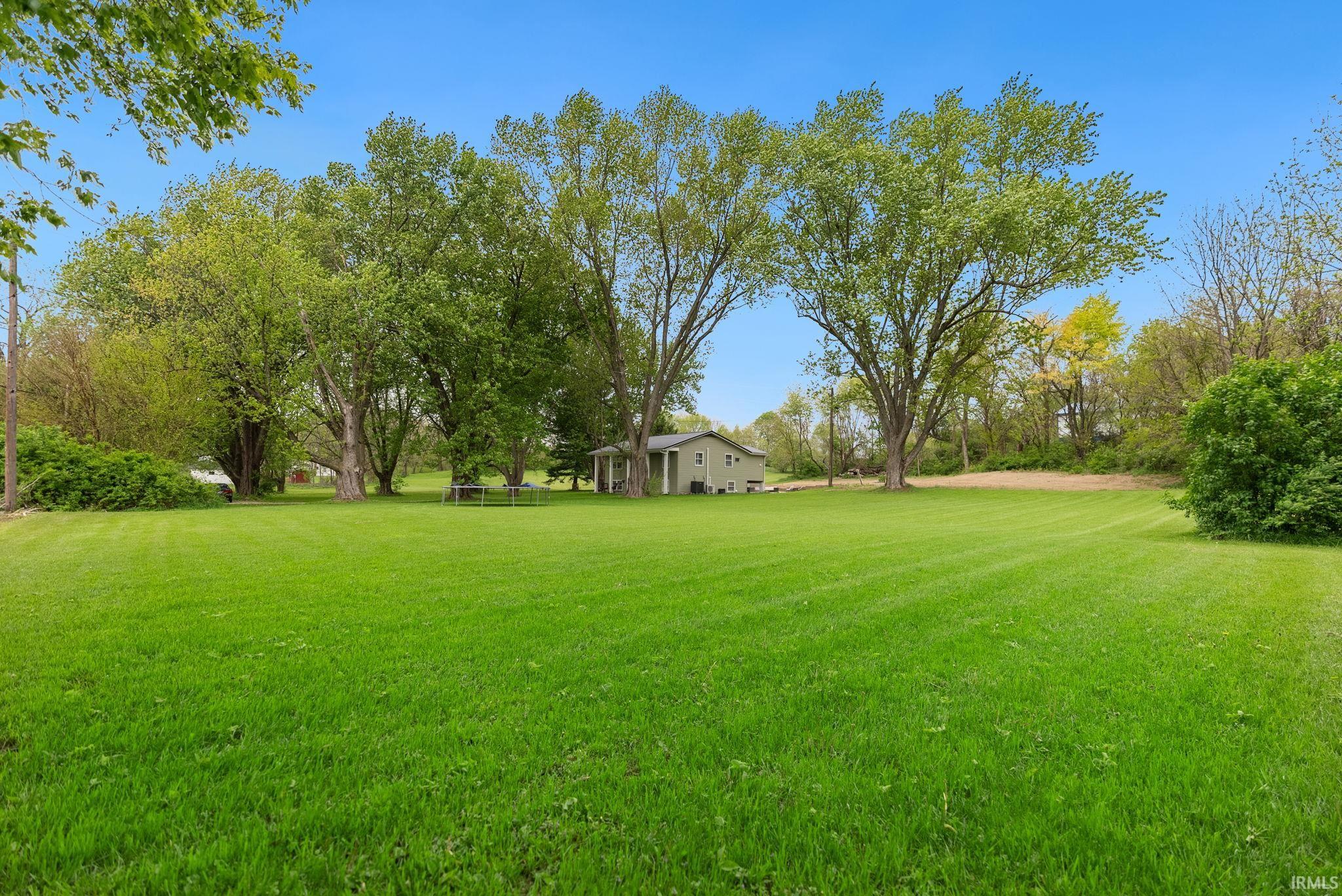 Spacious green lawn with mature trees providing extensive shade and a clear blue sky overhead